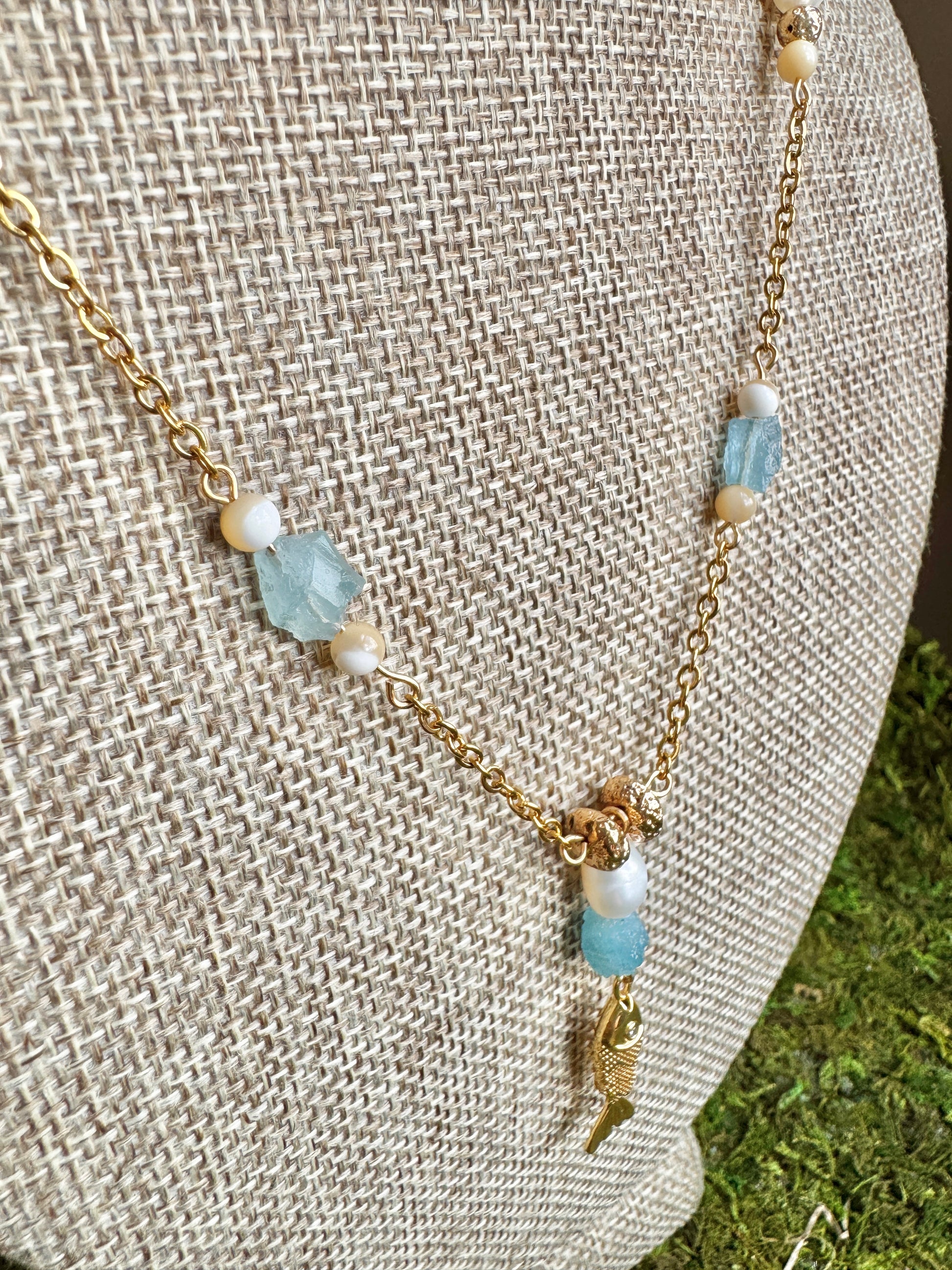 Necklace with gold chain and blue and white beads on a textured surface