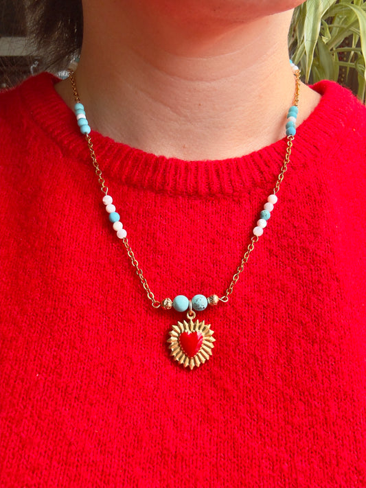 Red enamel gold stainless steel heart pendant on gold stainless steel chain with blue howlite and mother of pearl beads, close up on model