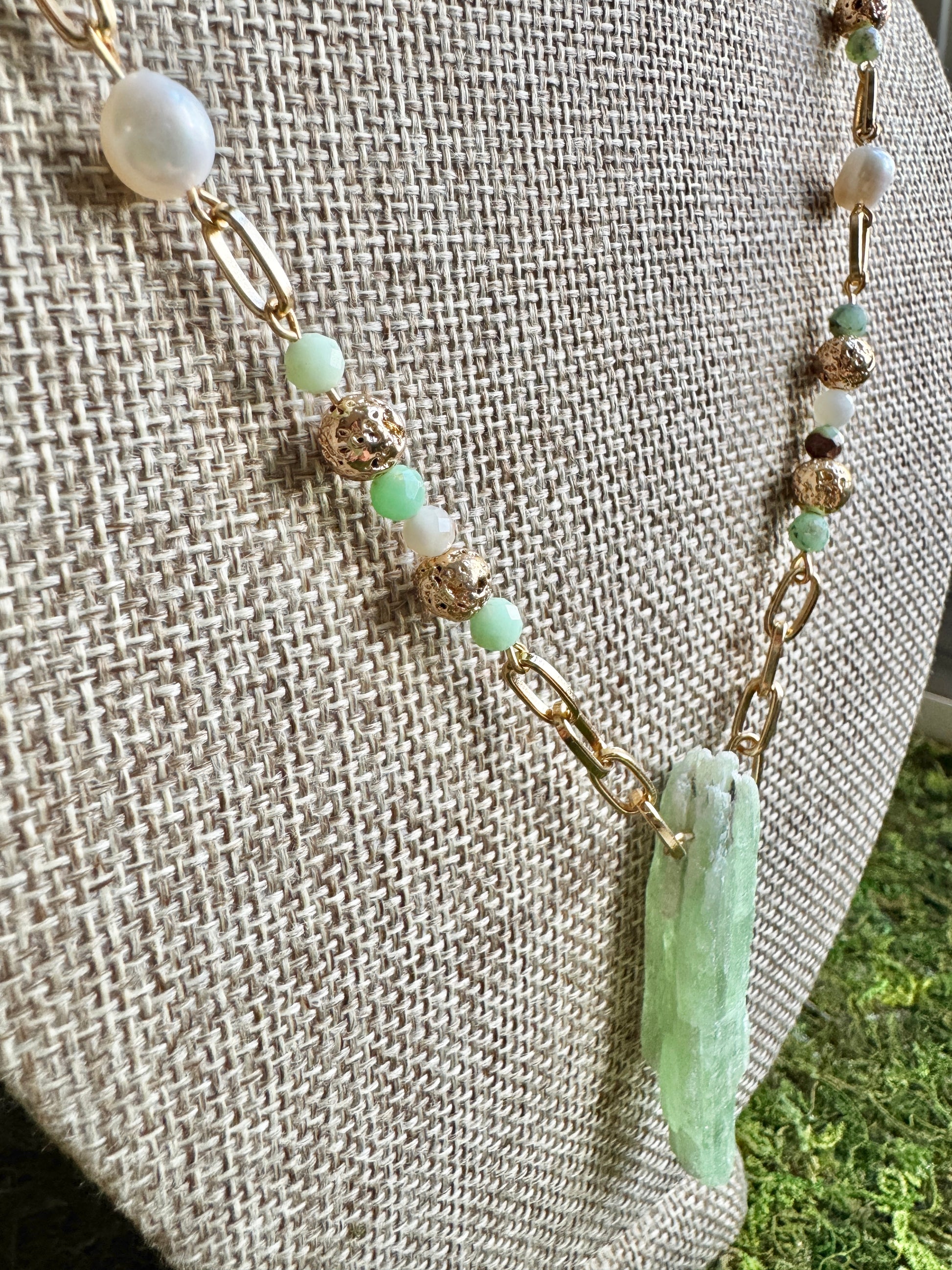 Necklace with green beads and a gold chain on a textured surface