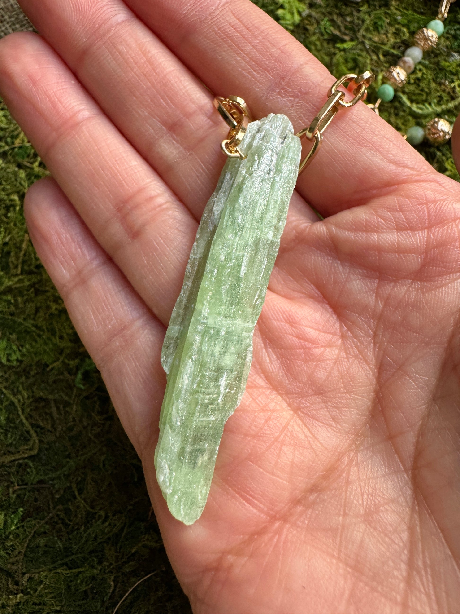 Crystal pendant on a gold chain held in a hand with a natural background