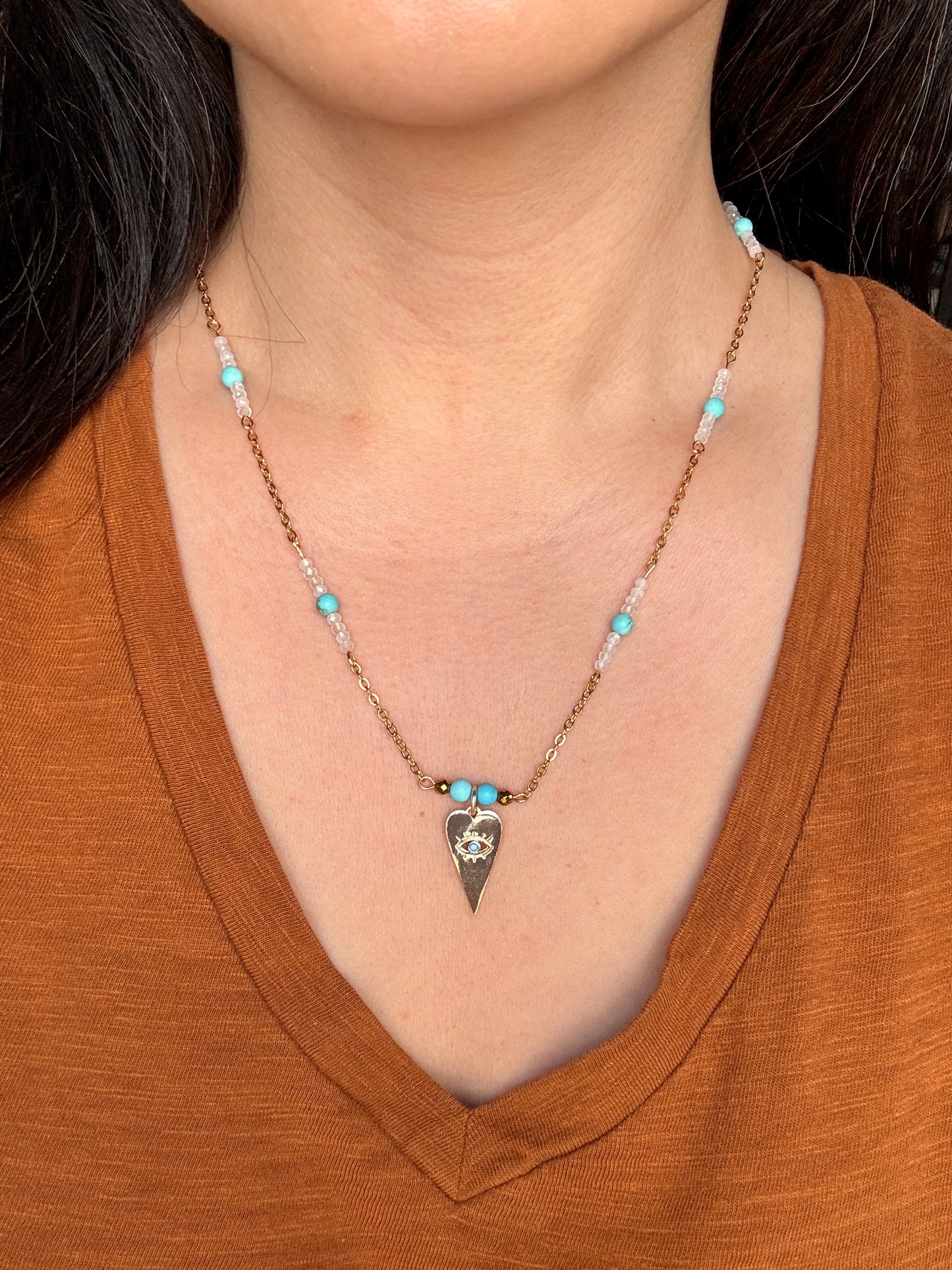 Necklace with a triangular pendant worn by a person in a brown shirt