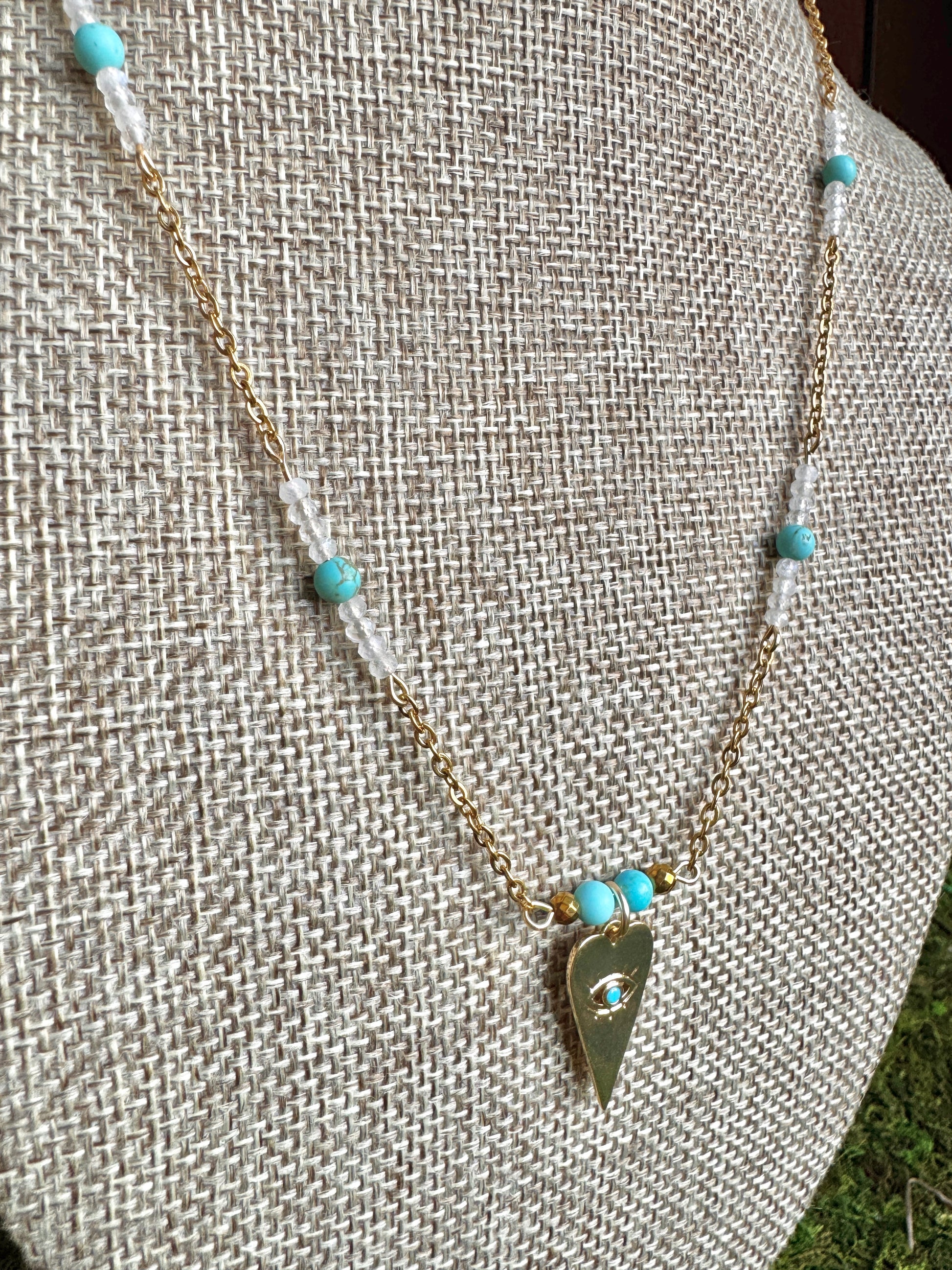 Necklace with turquoise beads and a gold triangle pendant on a textured surface.