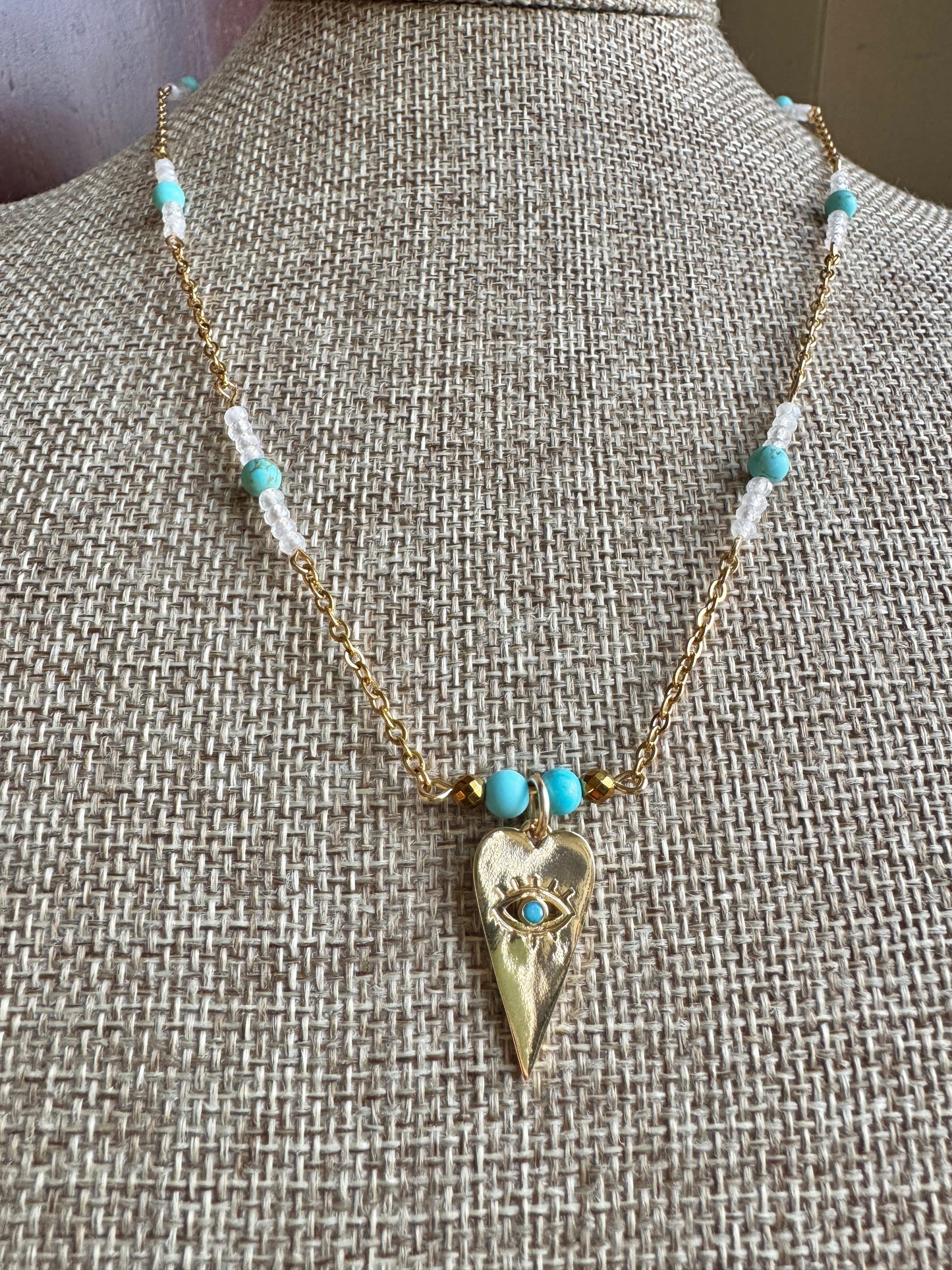 Necklace with turquoise beads and a gold pendant on a textured surface
