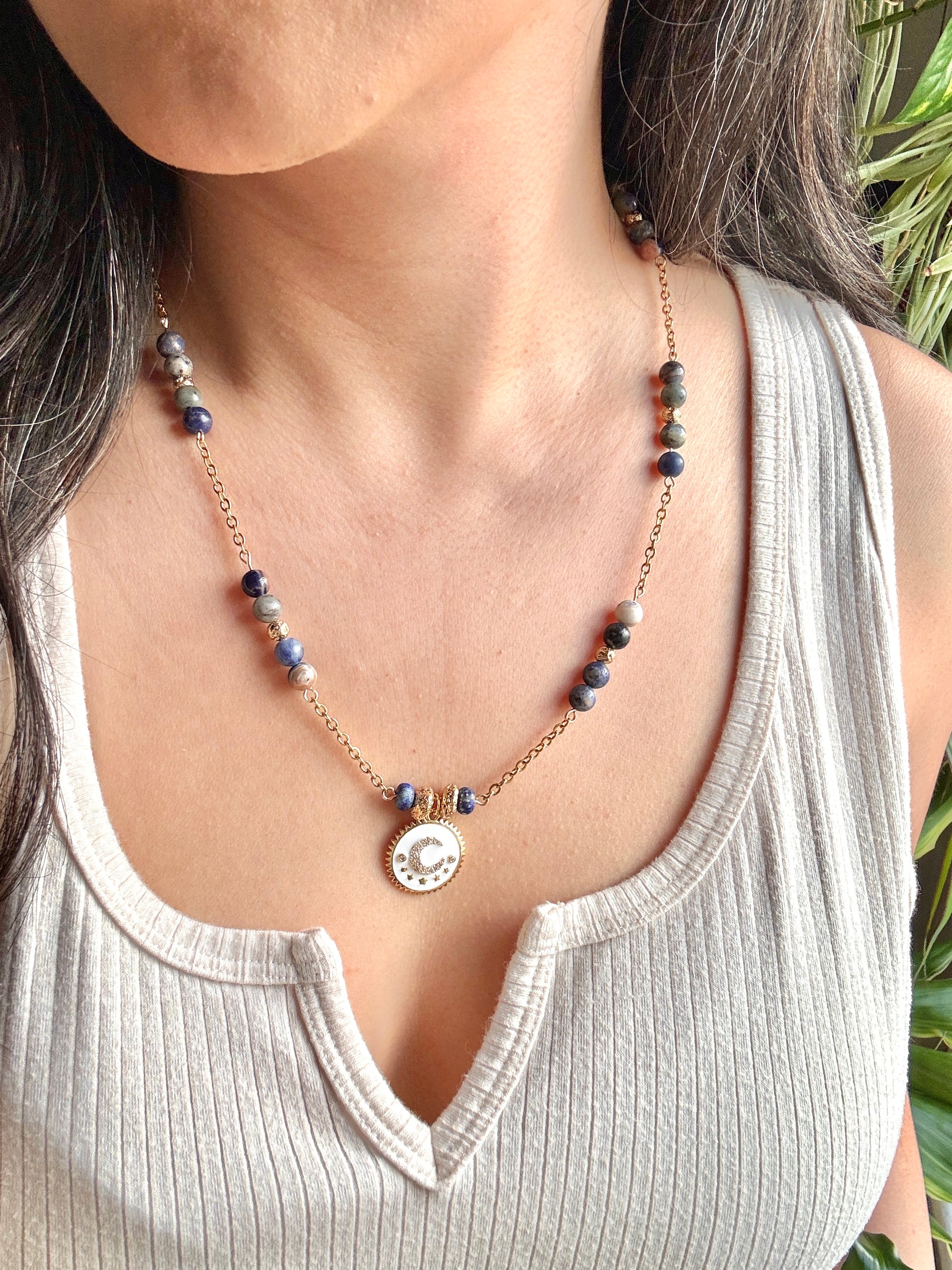 Necklace with beads and a circular pendant worn by a person in a white tank top.