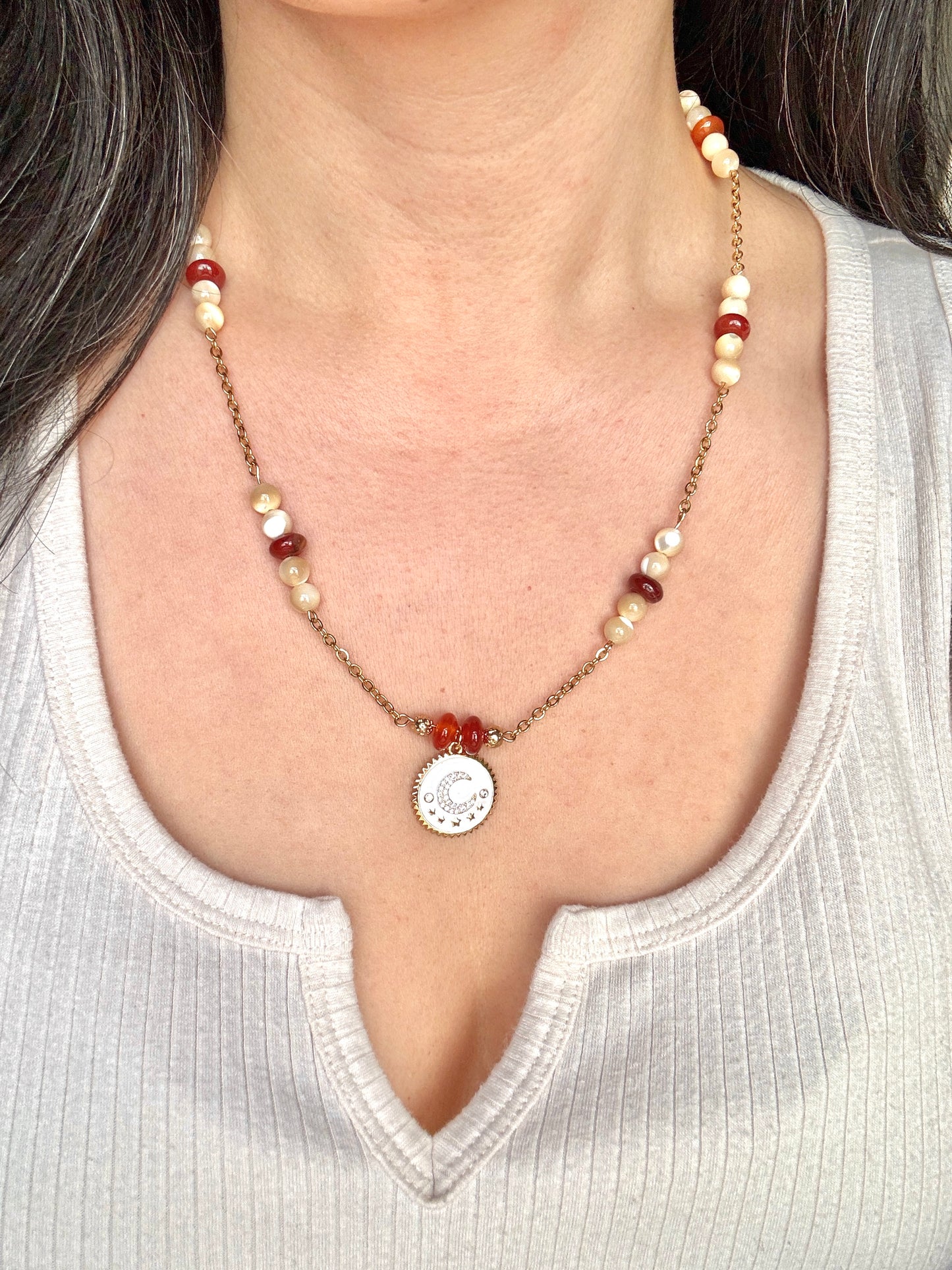Necklace with beads and a circular pendant worn by a person in a white top.