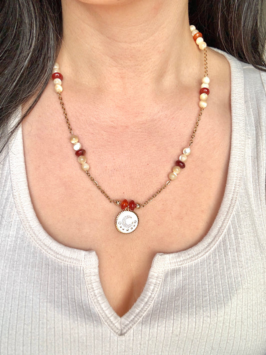 Necklace with beads and a circular pendant worn by a person in a white top.