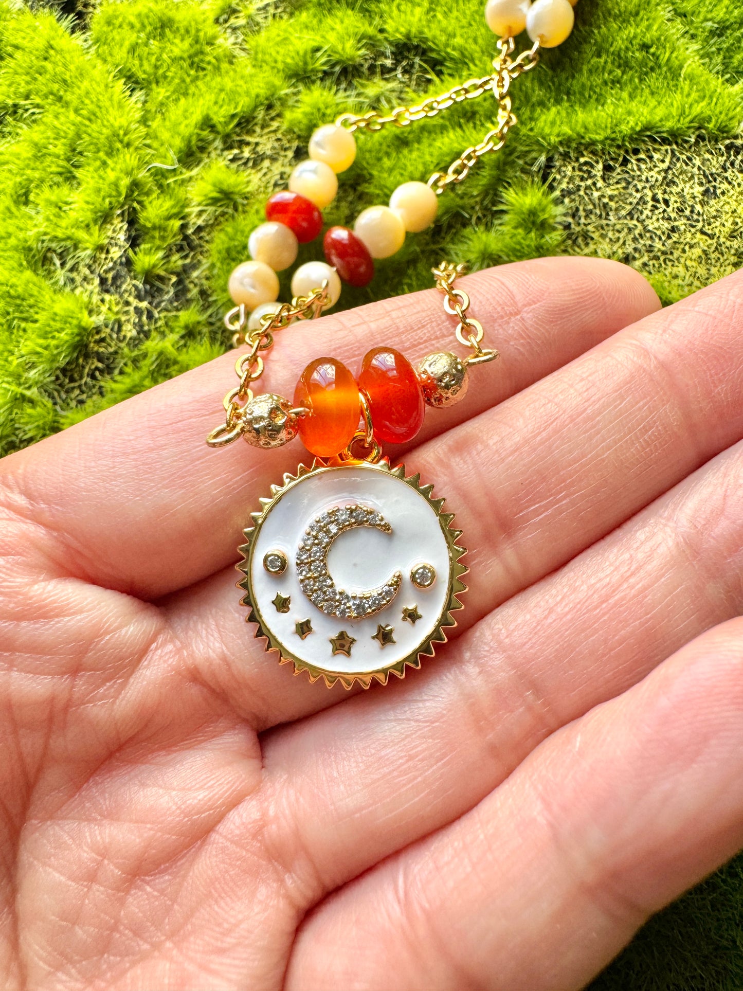 Necklace with a decorative pendant held in a hand against a green moss background