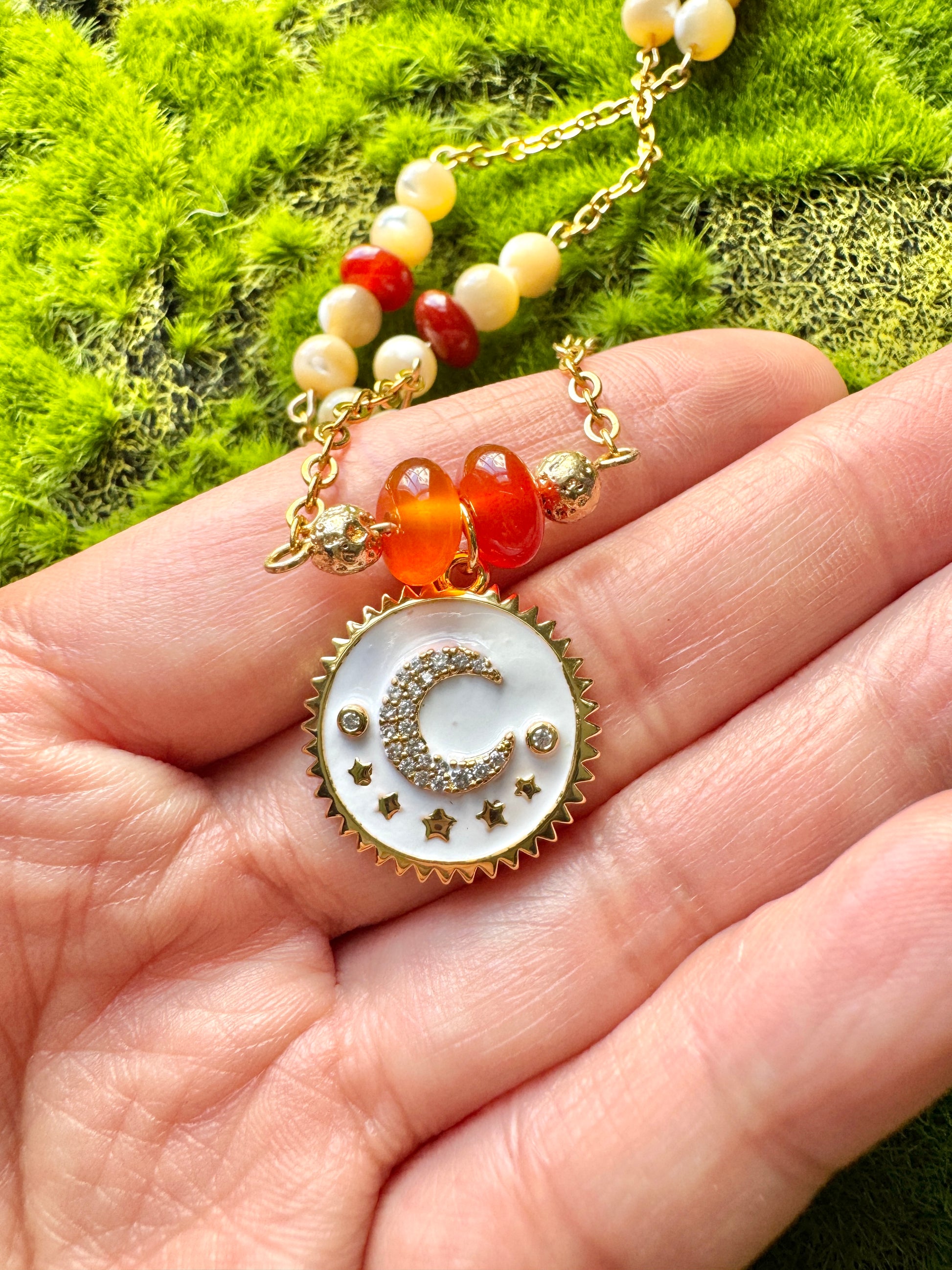 Necklace with a decorative pendant held in a hand against a green moss background