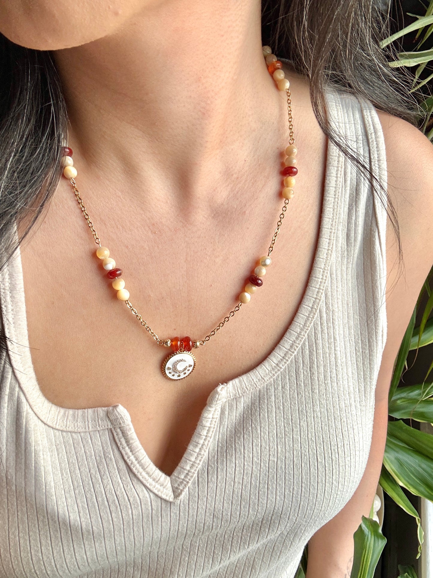 Necklace with a pendant worn by a person in a light-colored top, with a blurred natural background.