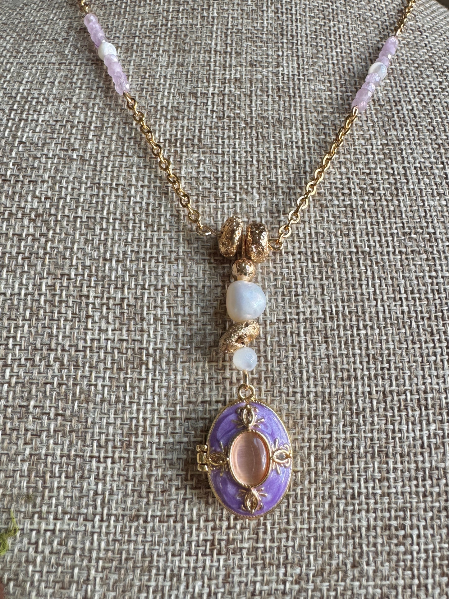 Necklace with a purple pendant and beaded chain on a textured fabric background