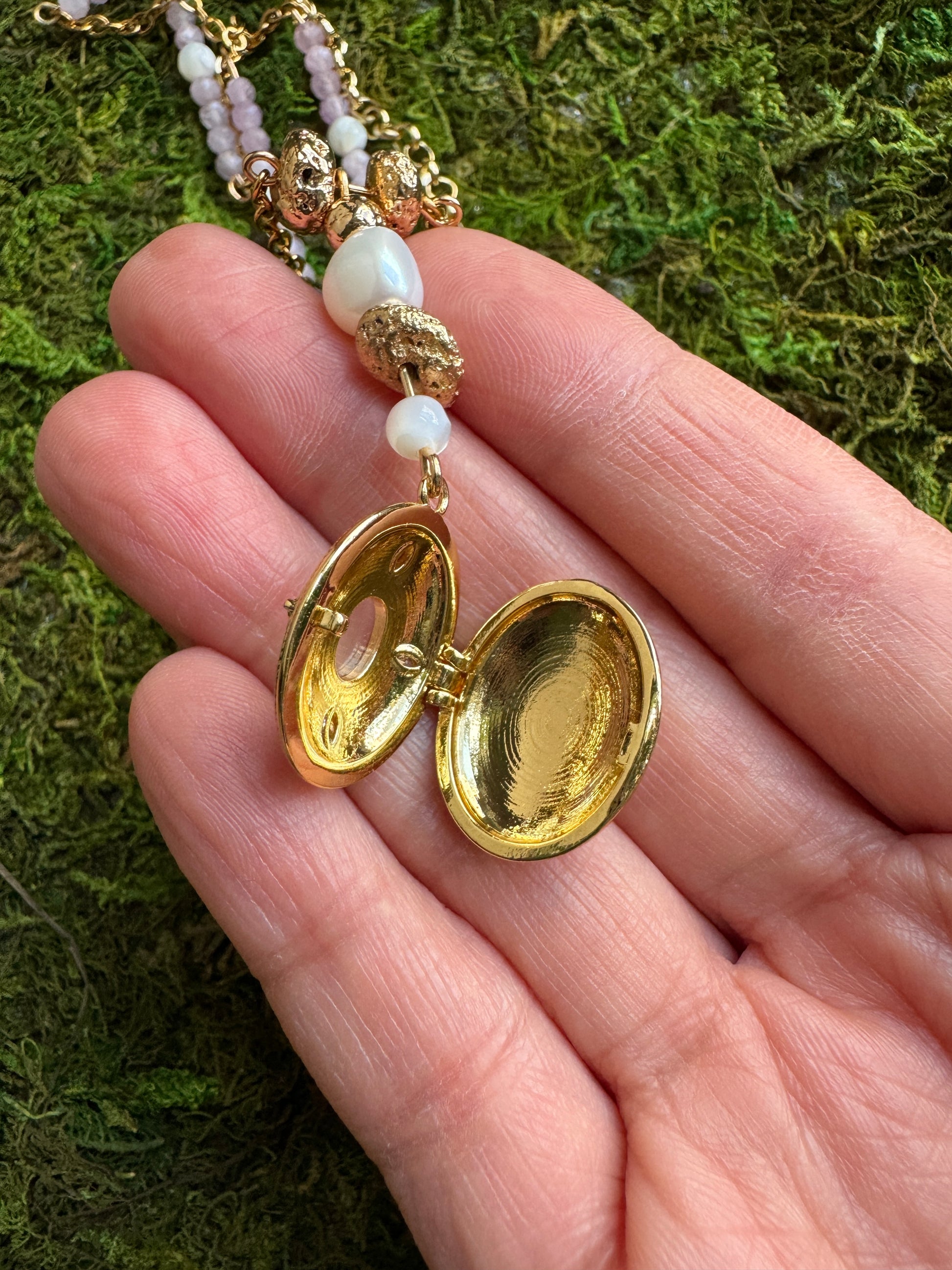 Gold locket with a hand holding it against a green moss background