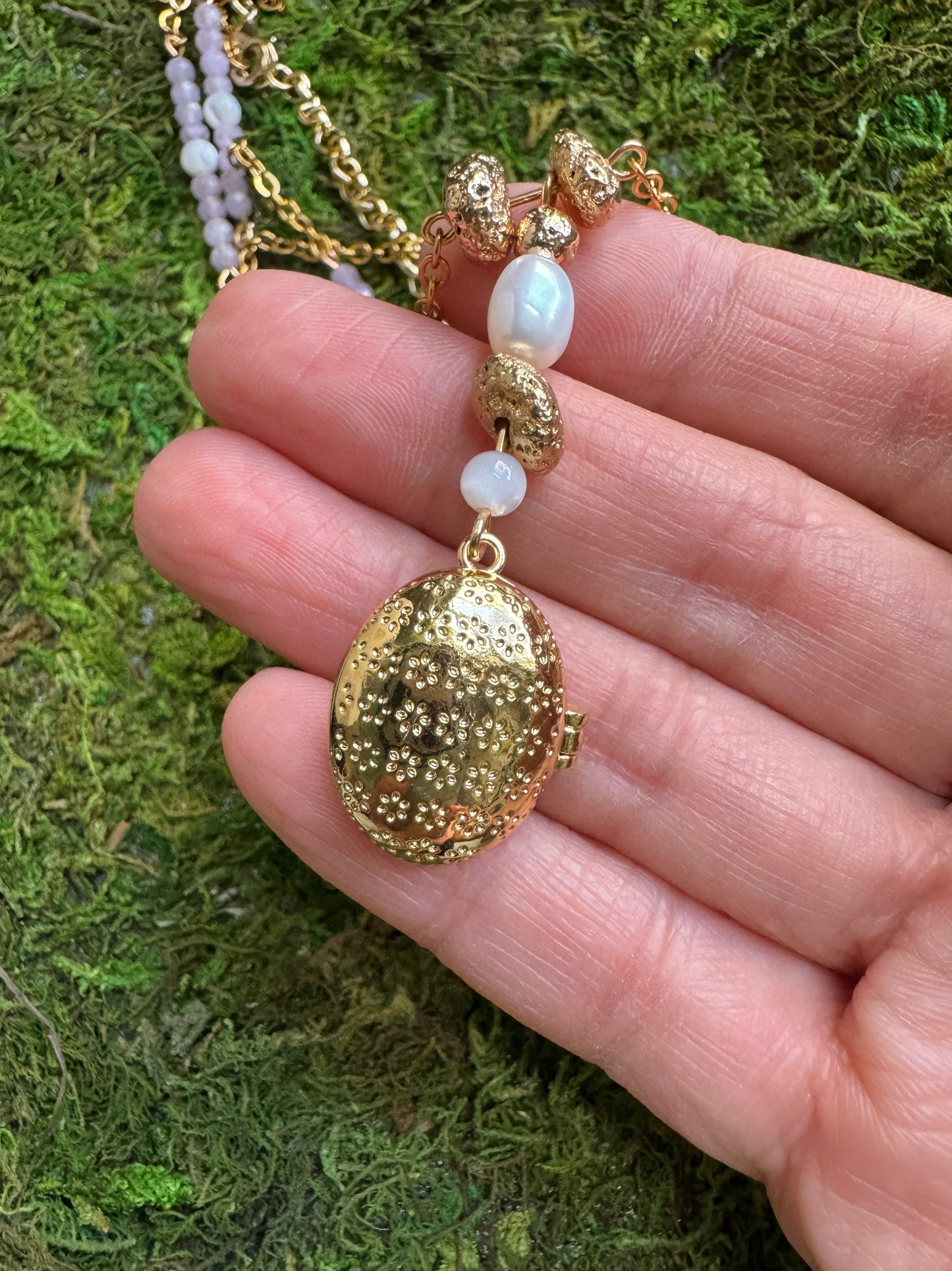 Gold pendant necklace with beads held by a hand on a green moss background