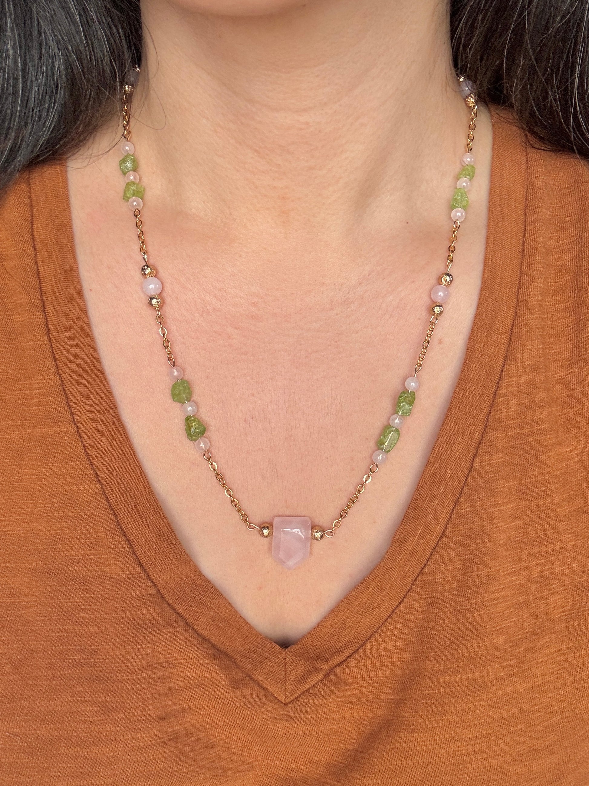 Necklace with green and pink beads worn by a person in a brown shirt