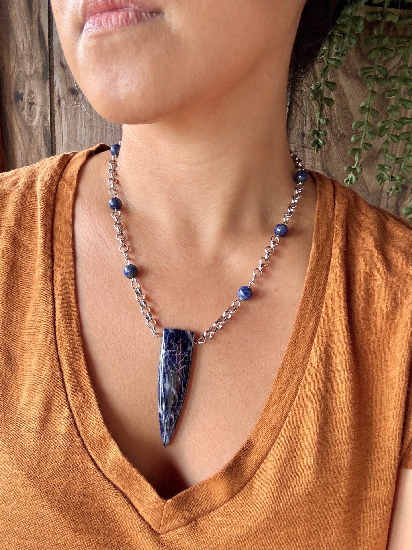 Necklace with a blue pendant worn by a person in an orange shirt against a wooden background