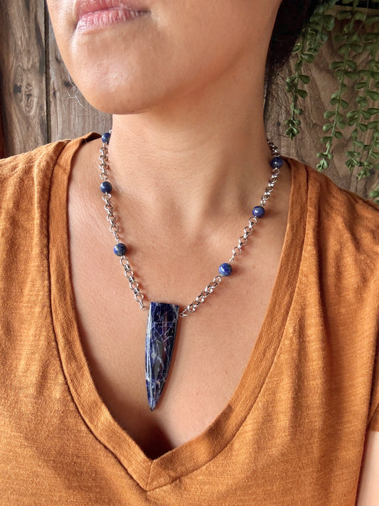 Necklace with a blue pendant worn by a person in an orange shirt against a wooden background