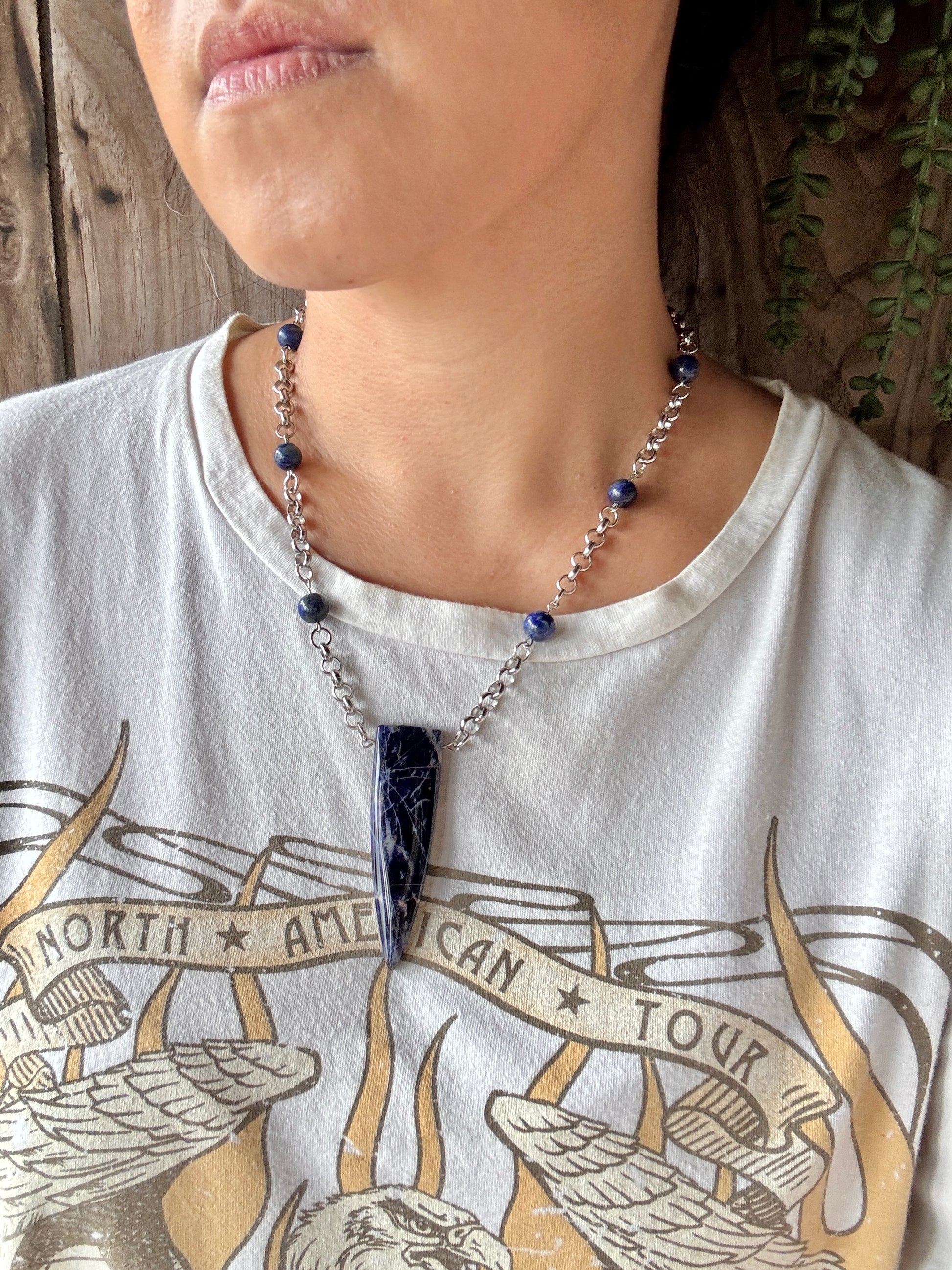 Person wearing a necklace with a blue pendant on a white t-shirt with printed design.