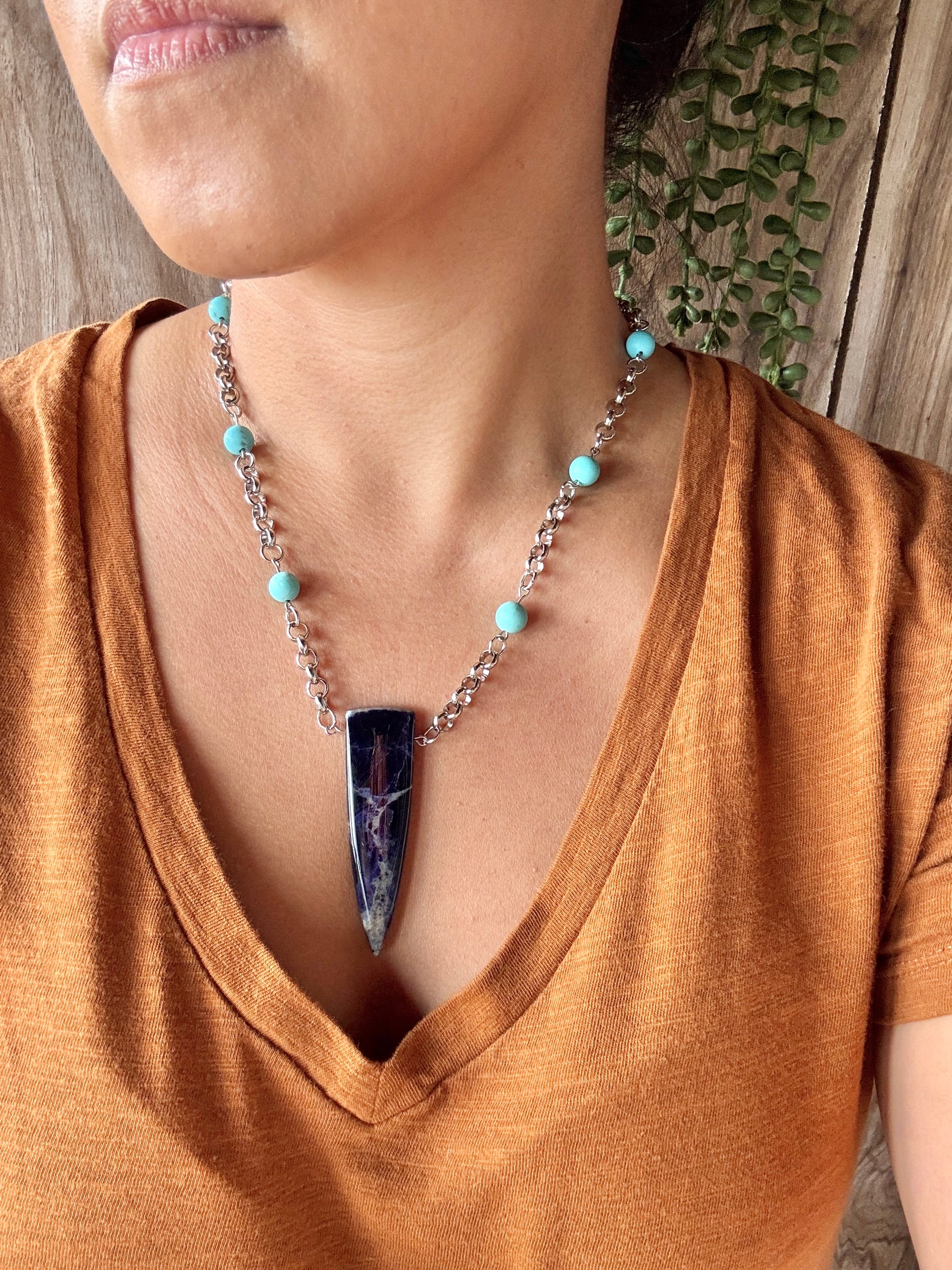 Necklace with a blue pendant worn by a person in a brown shirt.