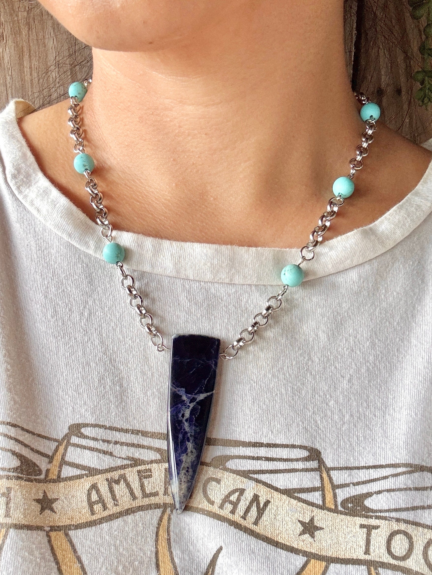 Necklace with turquoise beads and a dark pendant worn by a person on a white shirt.
