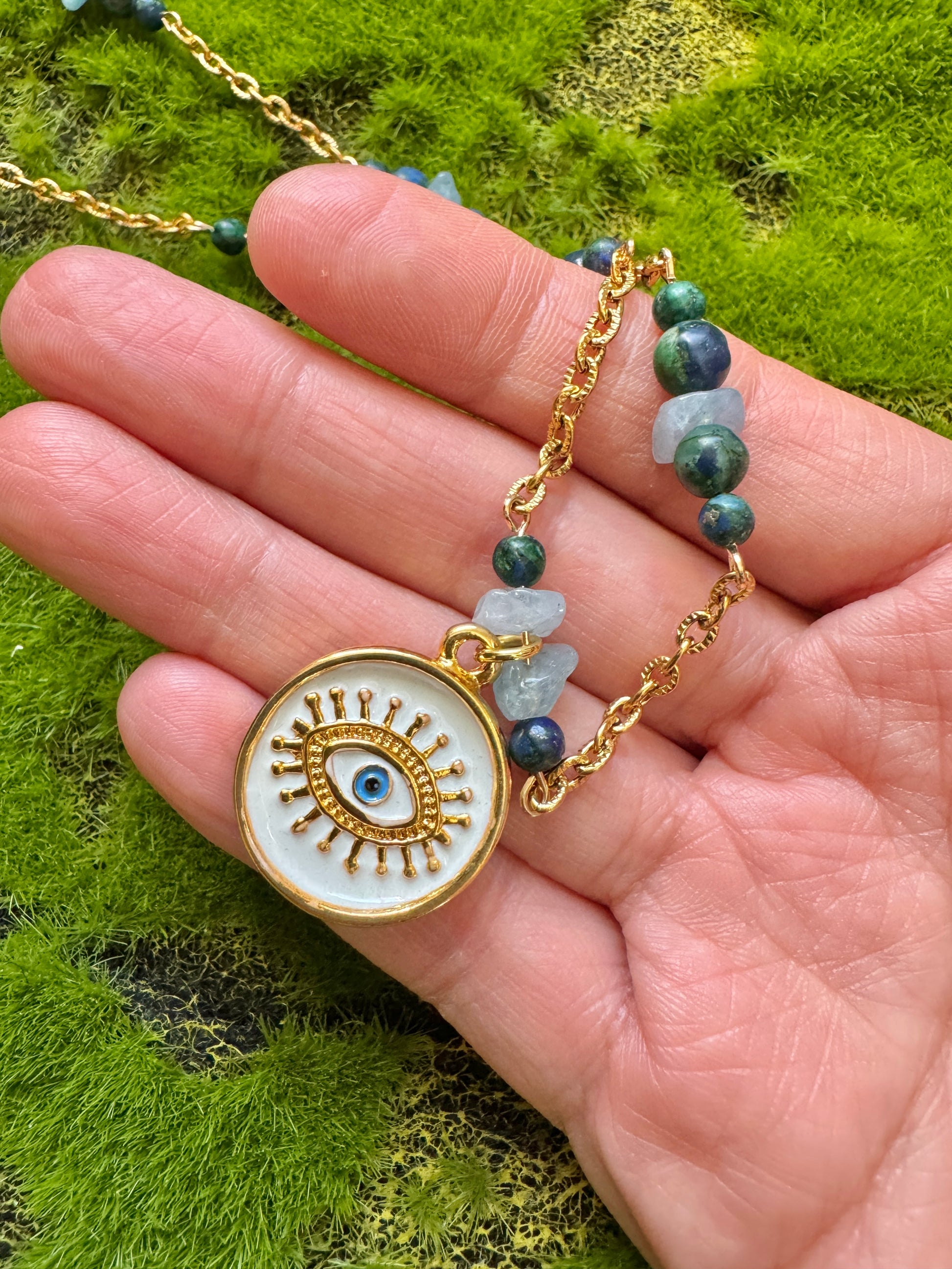 Eye pendant necklace close up in hand against a grass background