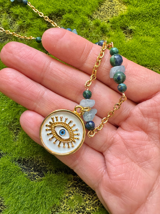 Eye pendant necklace close up in hand against a grass background