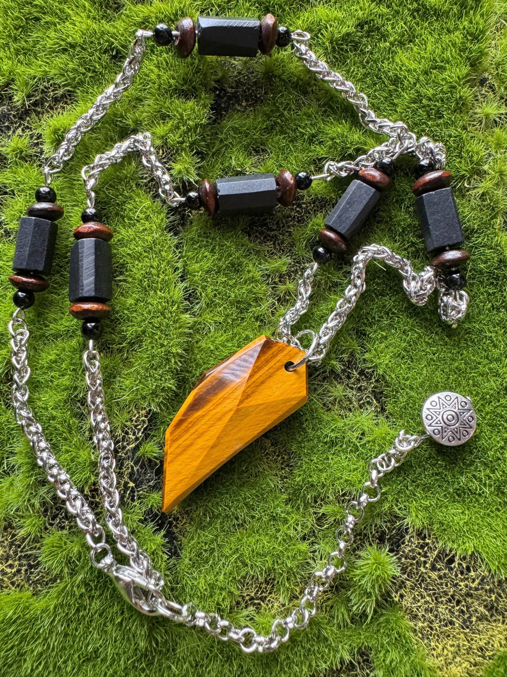 Necklace with wooden pendant and black beads on a green moss background