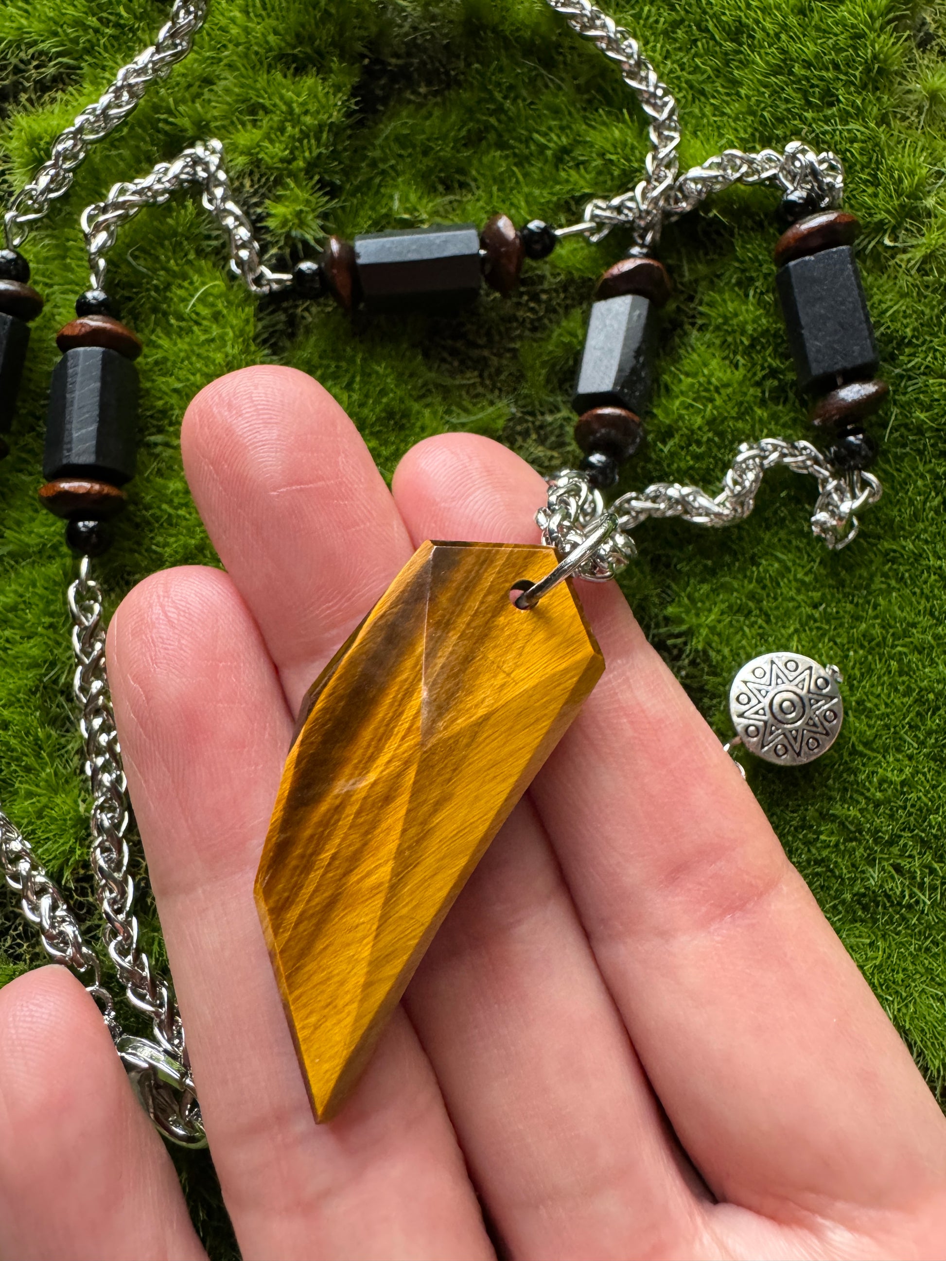 Hand holding a wooden pendant with a chain on a grassy background