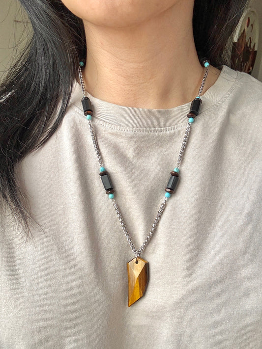 Necklace with wooden pendant and black and turquoise beads worn by a person on a plain background