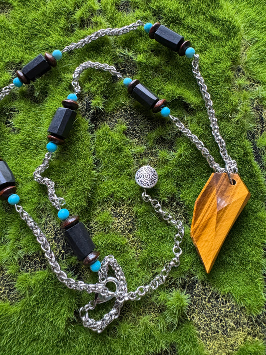 Necklace with black beads and blue accents on a chain, placed on green grass.