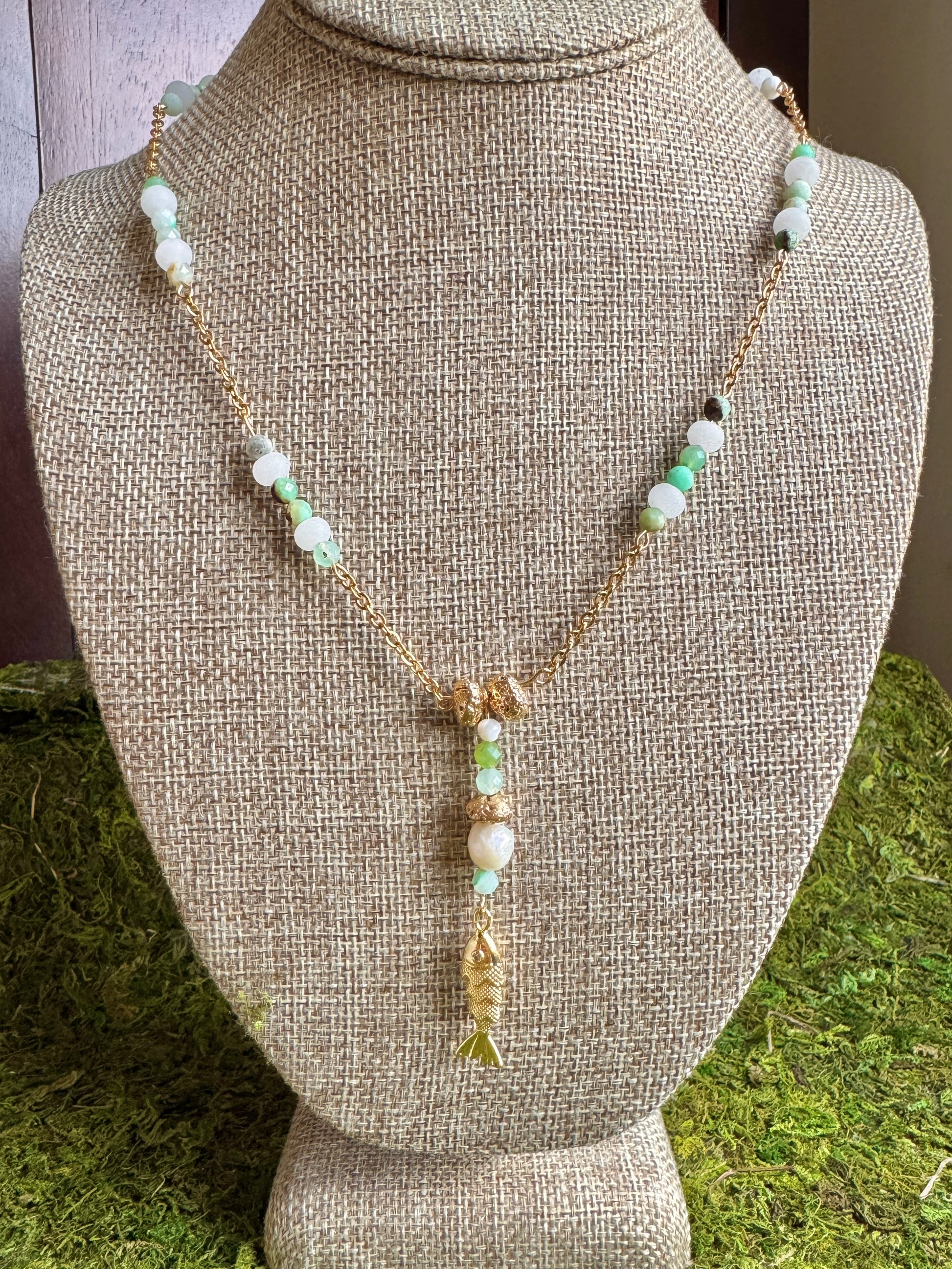 Necklace with fish pendant on a mannequin bust against a grassy background