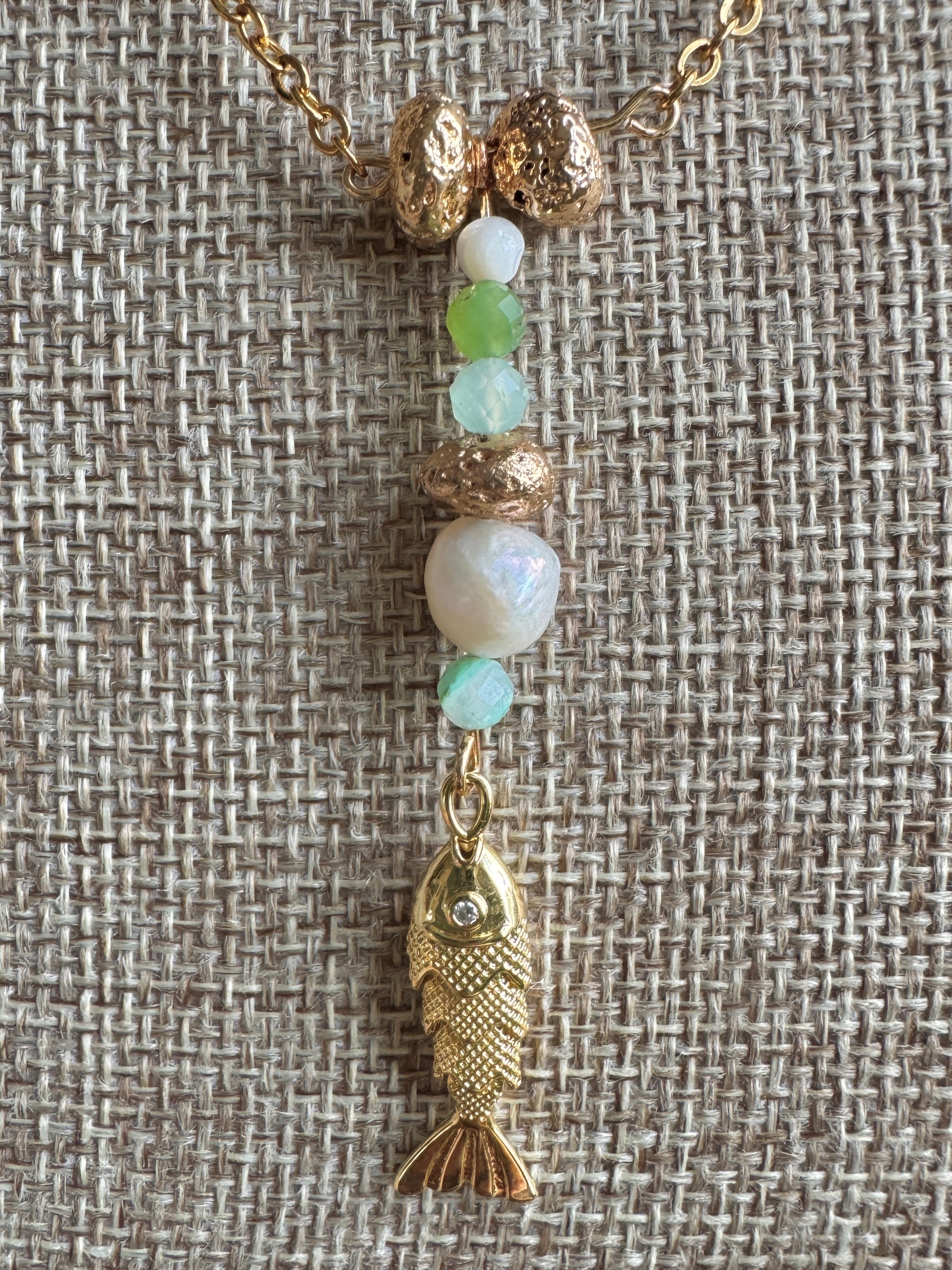 Necklace with gold fish charm and multicolored beads on a textured fabric background