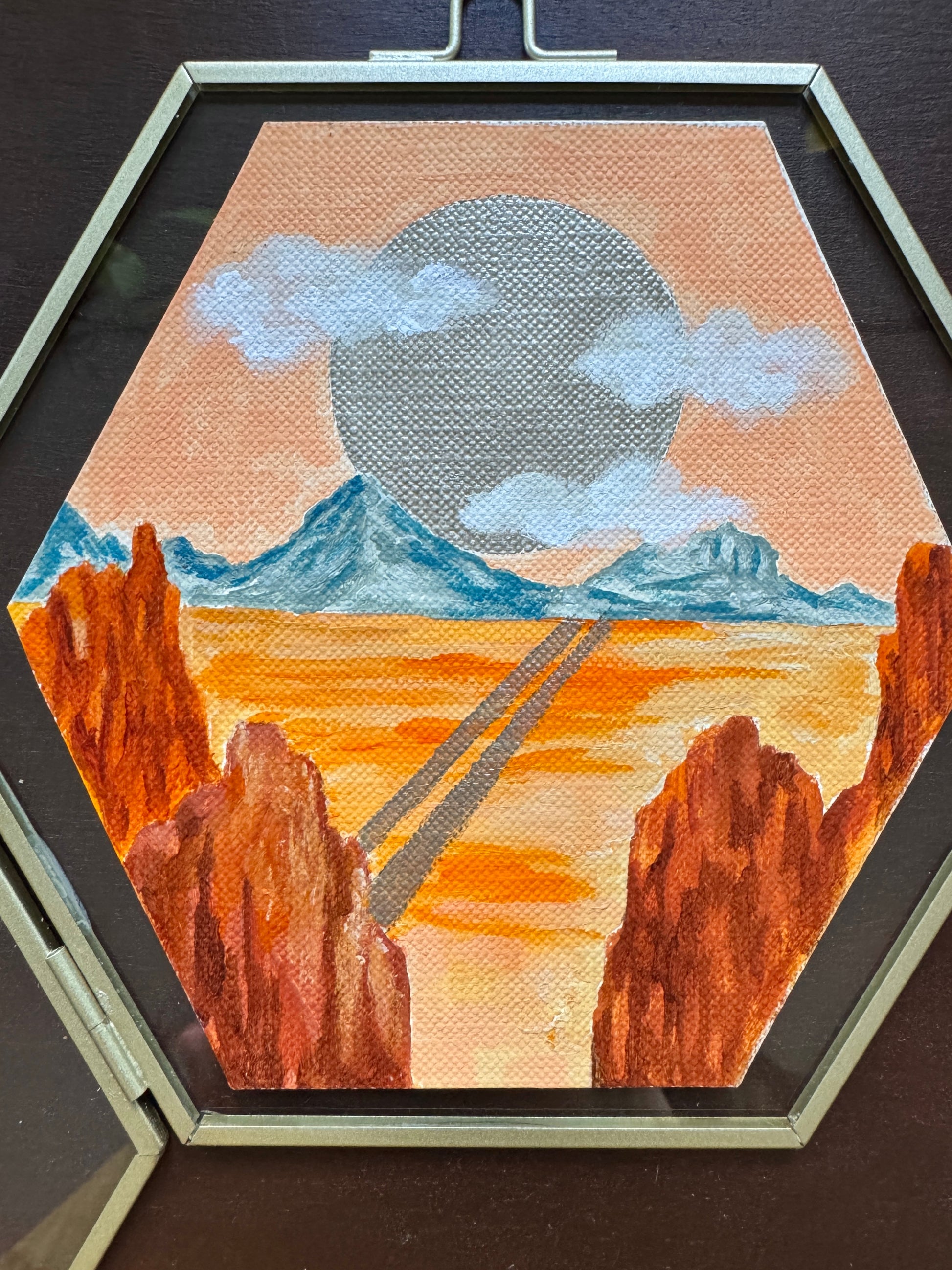 Desert landscape painting in glass frame against a wood background