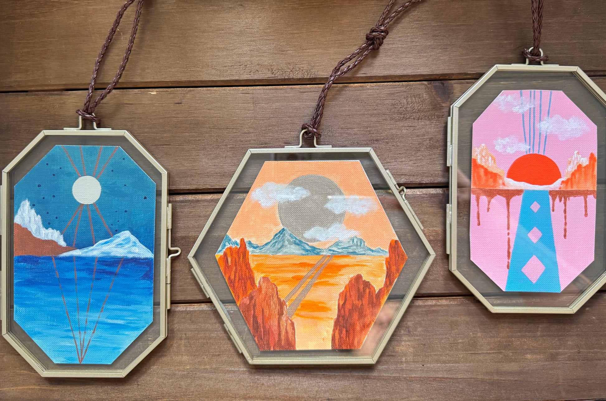 Set of three geometric glass framed landscape paintings against a wood background