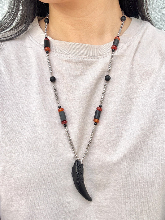Necklace with black and red beads and a large black pendant worn by a person on a white shirt.