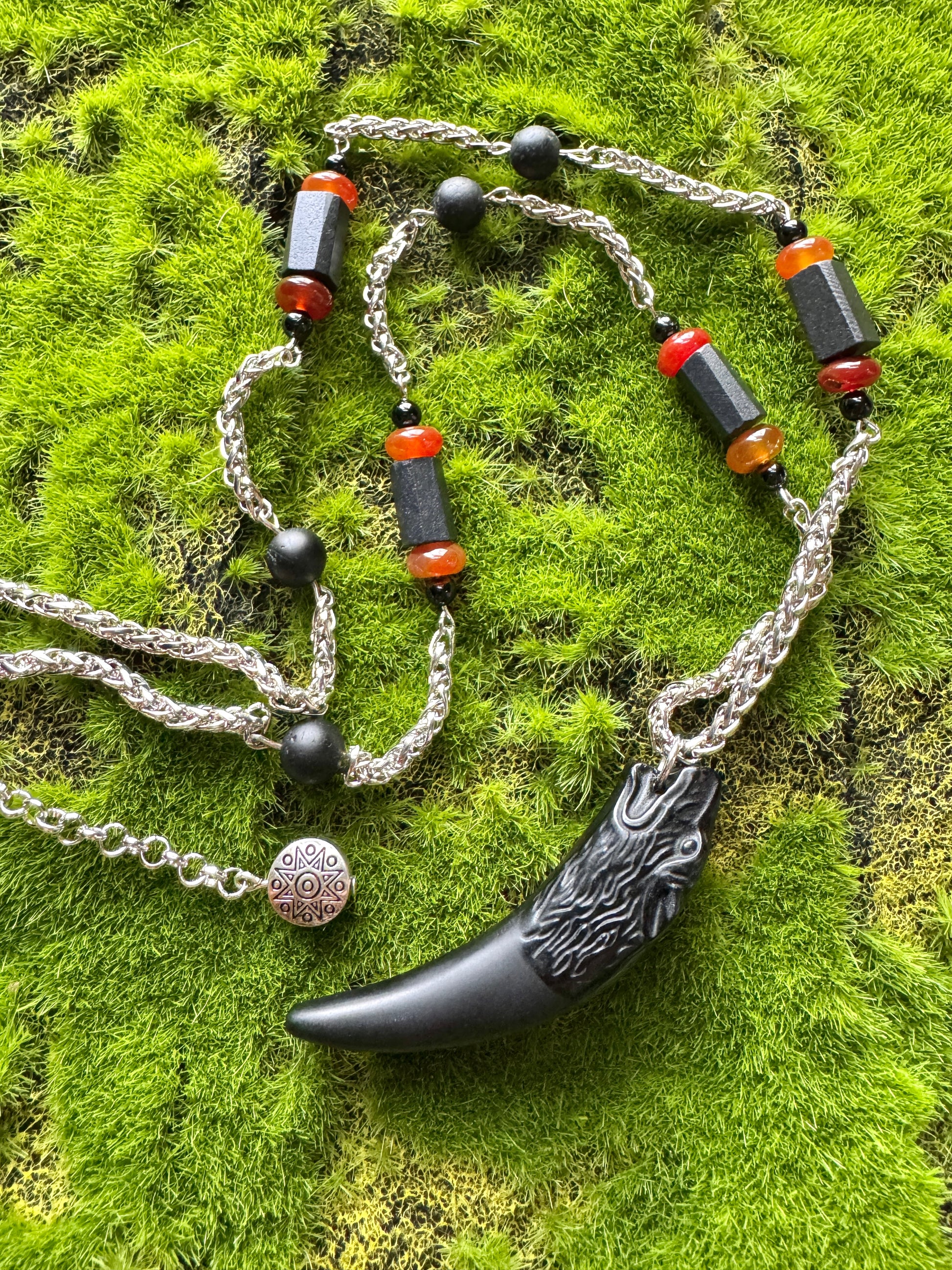 Necklace with black and red beads and a black pendant on a green moss background