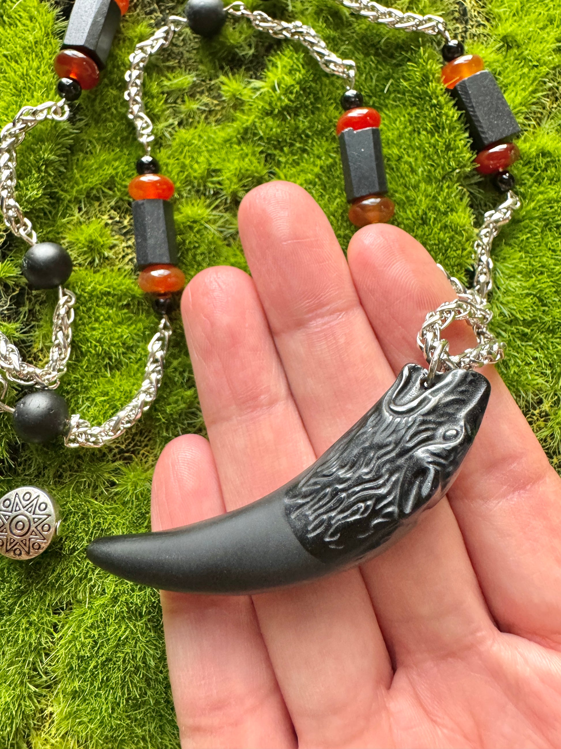 Hand holding a black and silver pendant with a chain on a green moss background