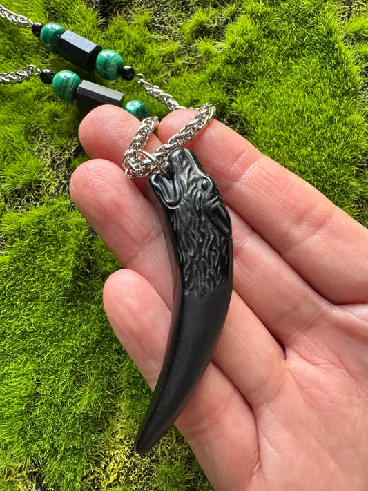 Hand holding a black and silver pendant against a green moss background