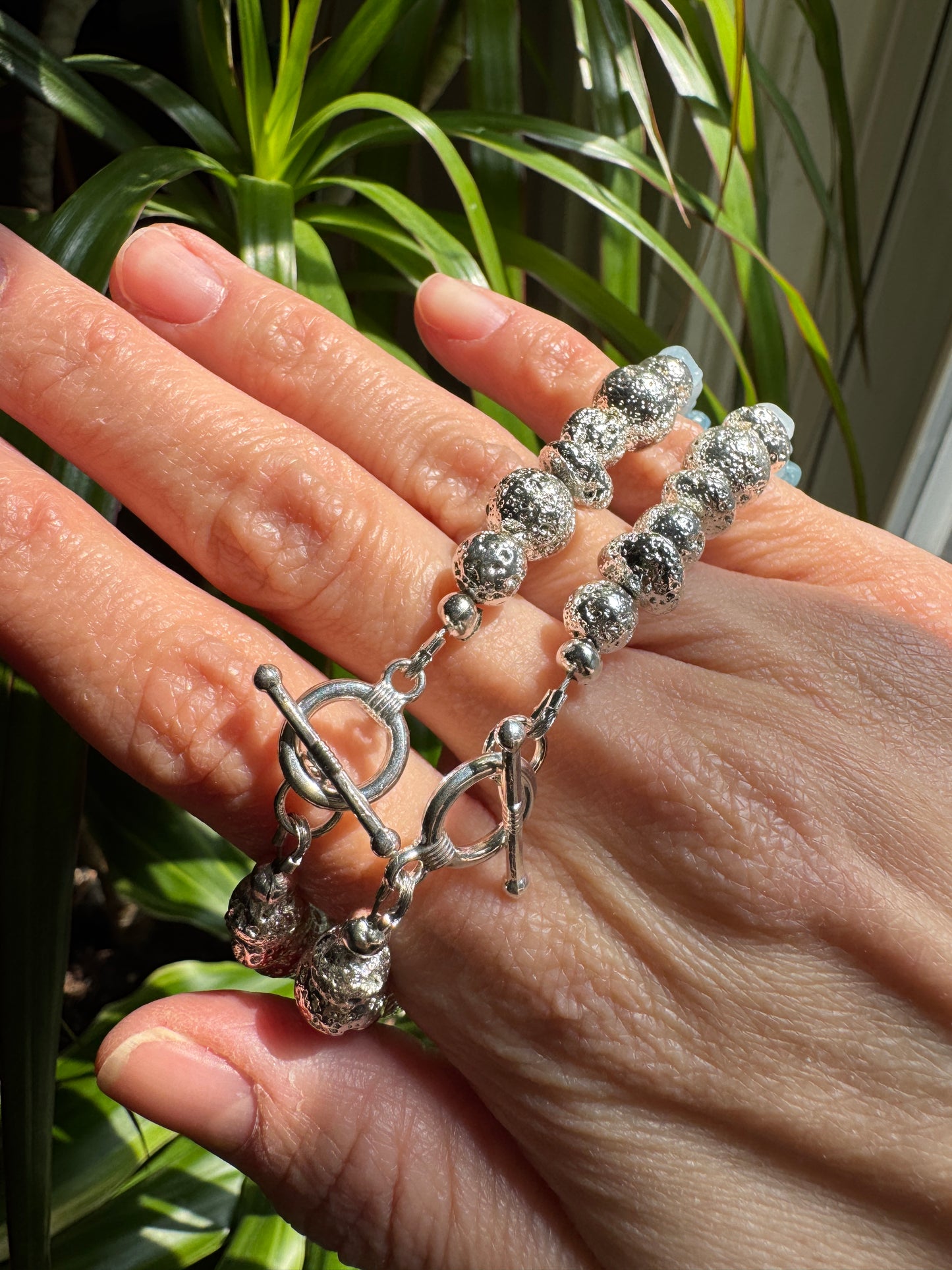 Silver beaded bracelet on a hand against a plant background
