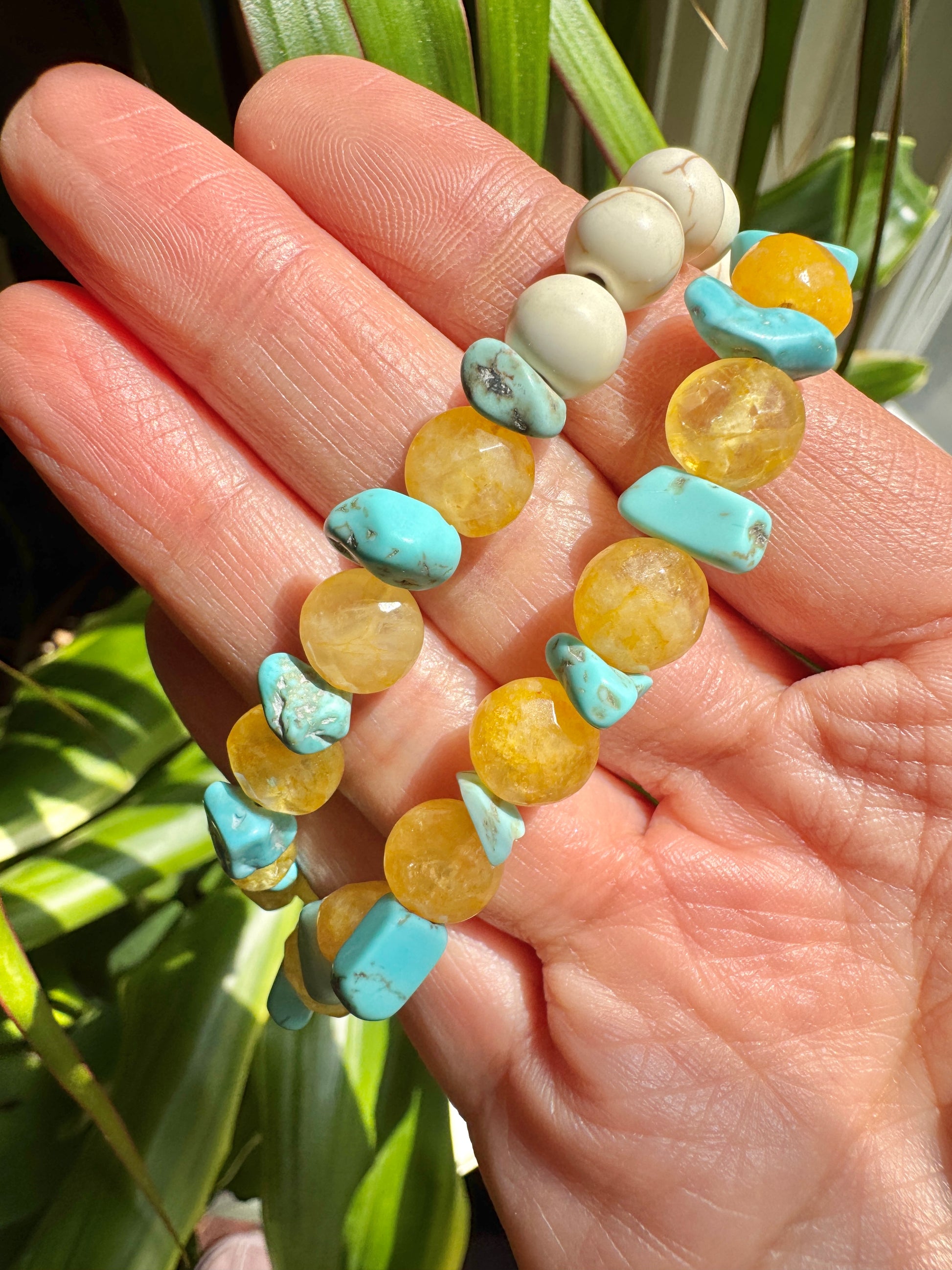 Hand holding a colorful beaded bracelet with a blurred green plant background