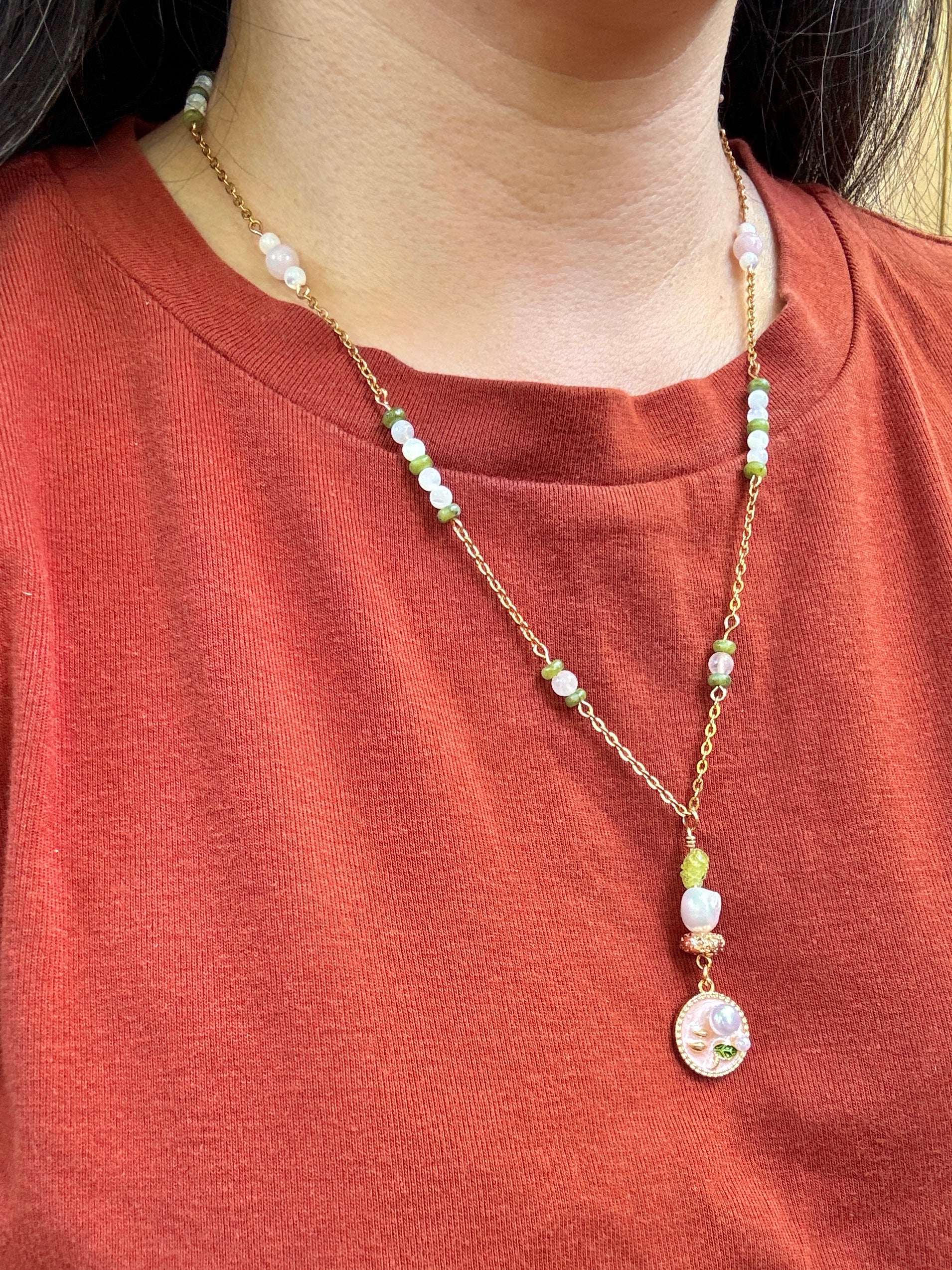 Necklace with beads and a pendant worn by a person on a red shirt