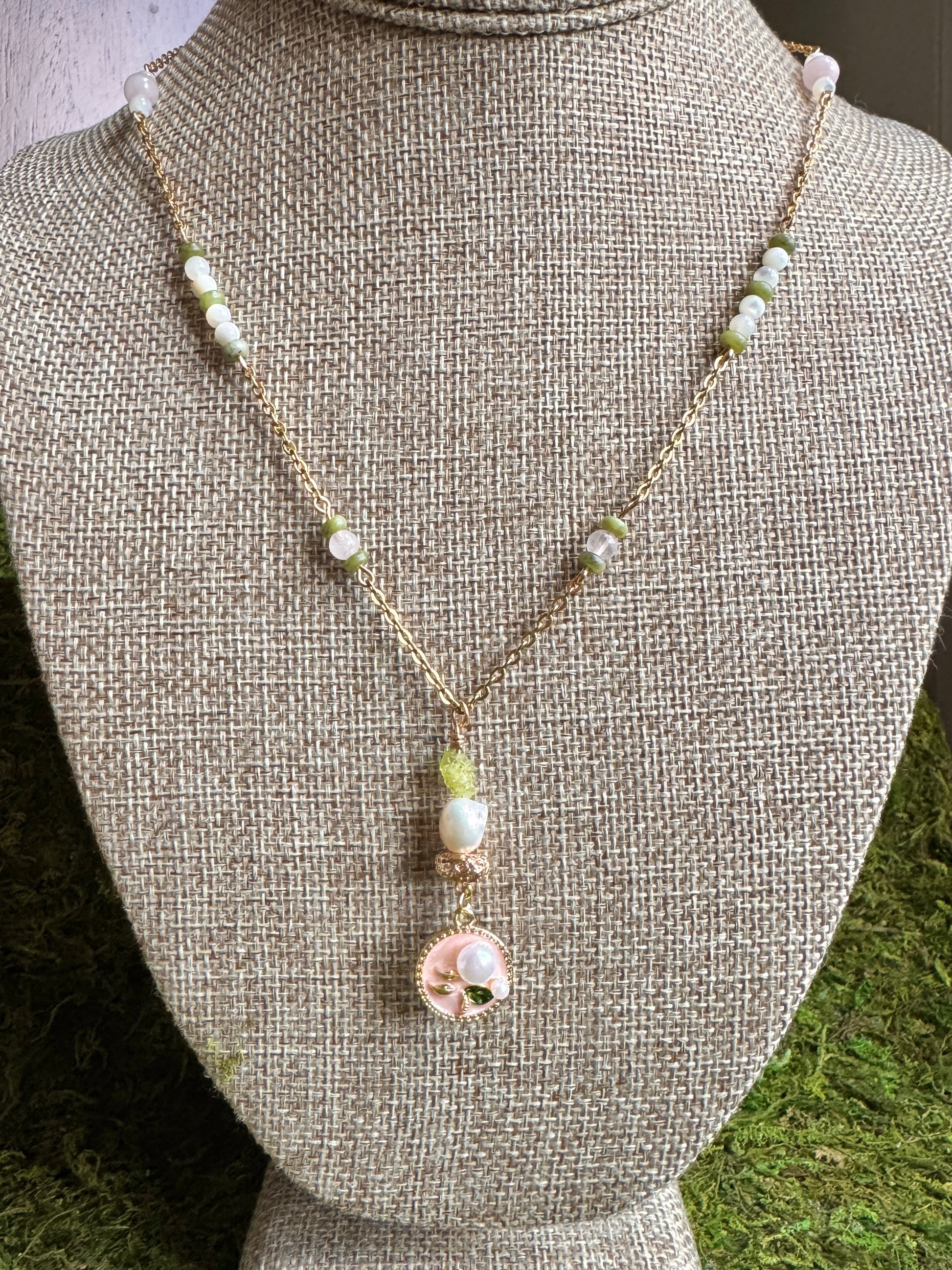 Necklace with pearls and a pink pendant on a mannequin bust.