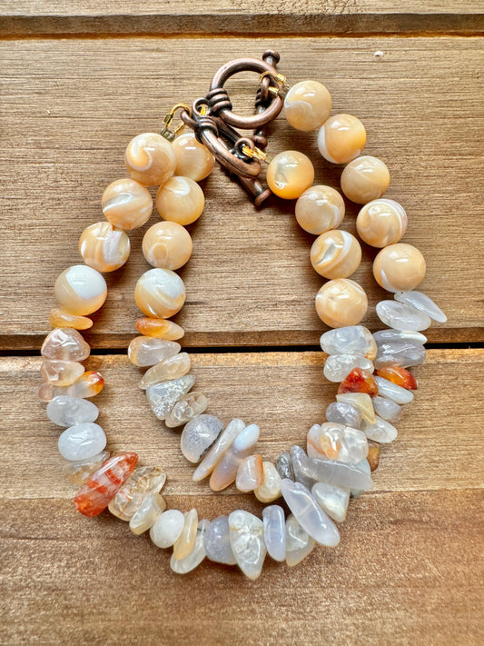 A bracelet with beads that appear to be made of Flower Agate and Mother of Pearl, featuring a toggle closure.