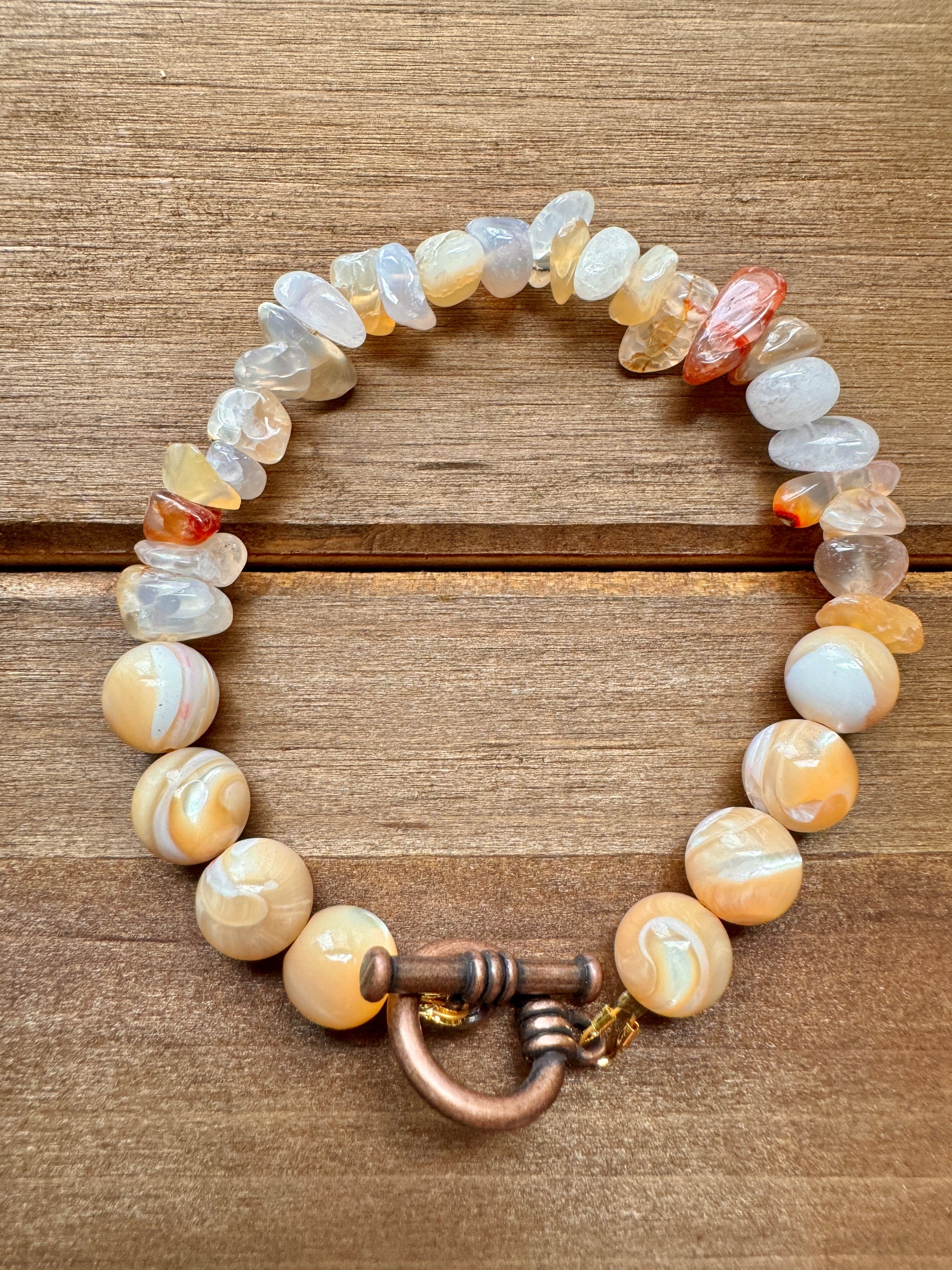 A bracelet with beads that appear to be made of Flower Agate and Mother of Pearl, featuring a toggle closure.