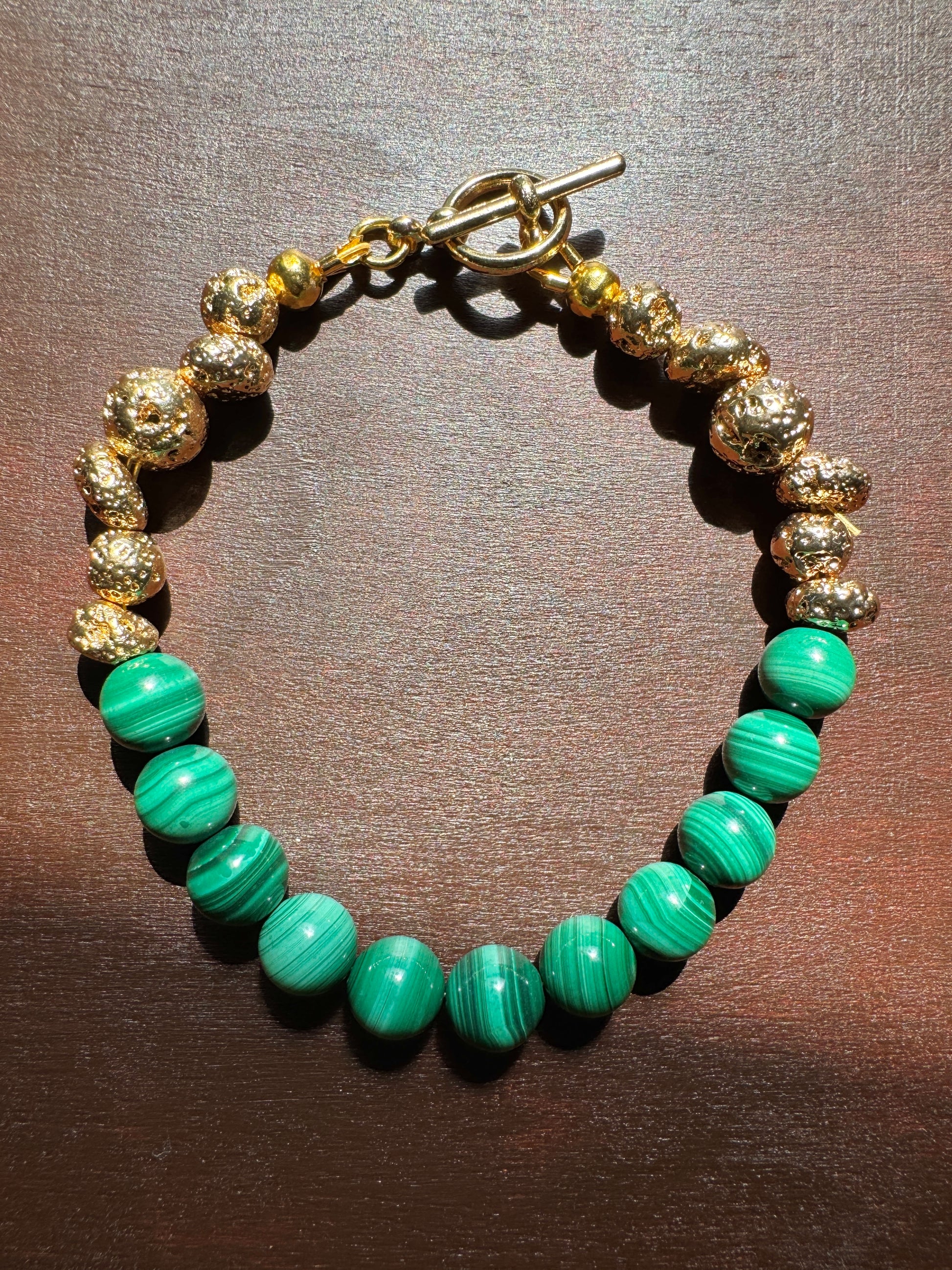 Bracelet with gold beads and green stones on a brown surface