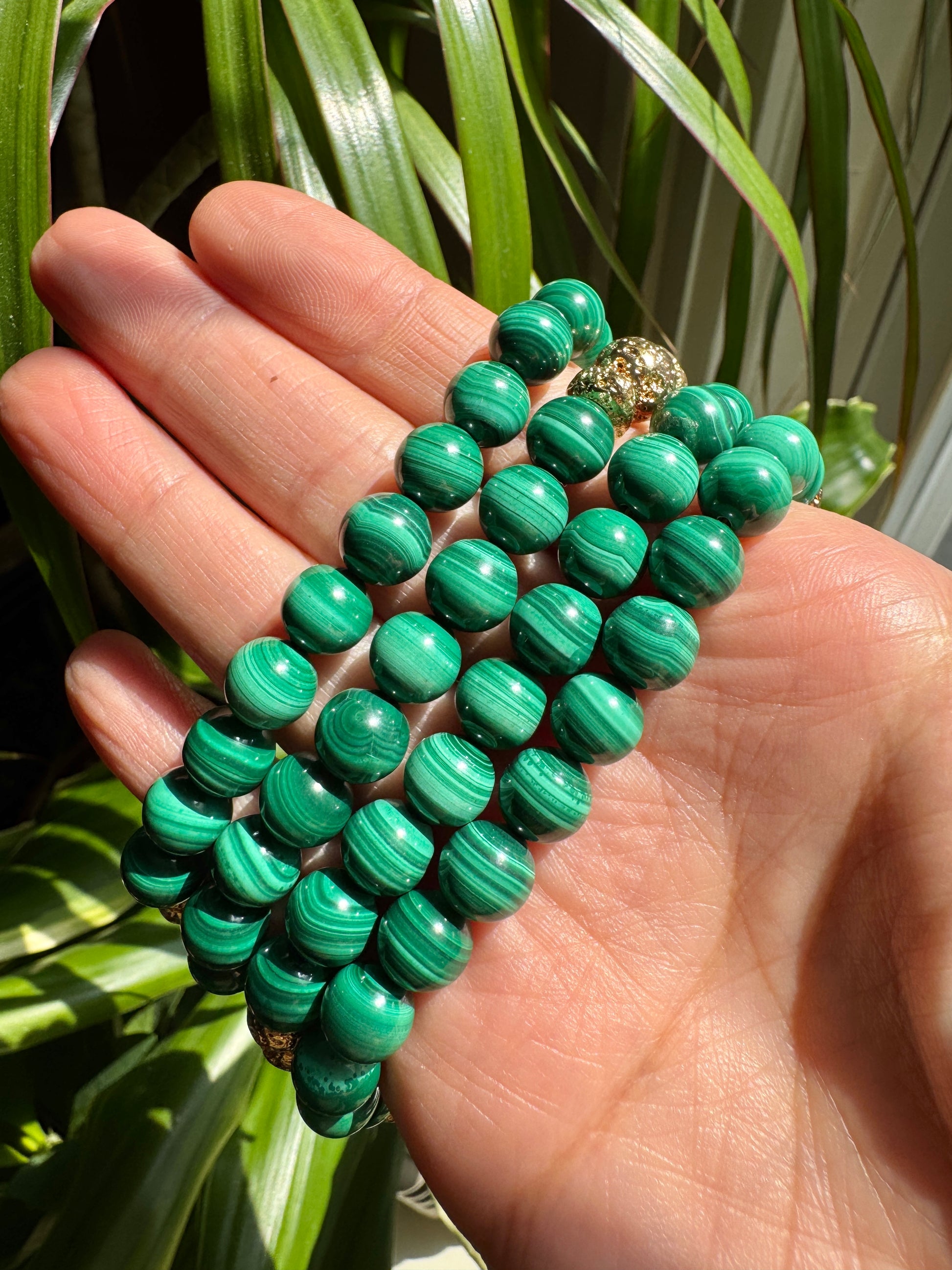 Green beaded bracelet held in a hand with a plant in the background