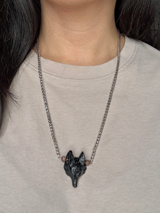 Necklace with wolf pendant worn by a person on a plain background